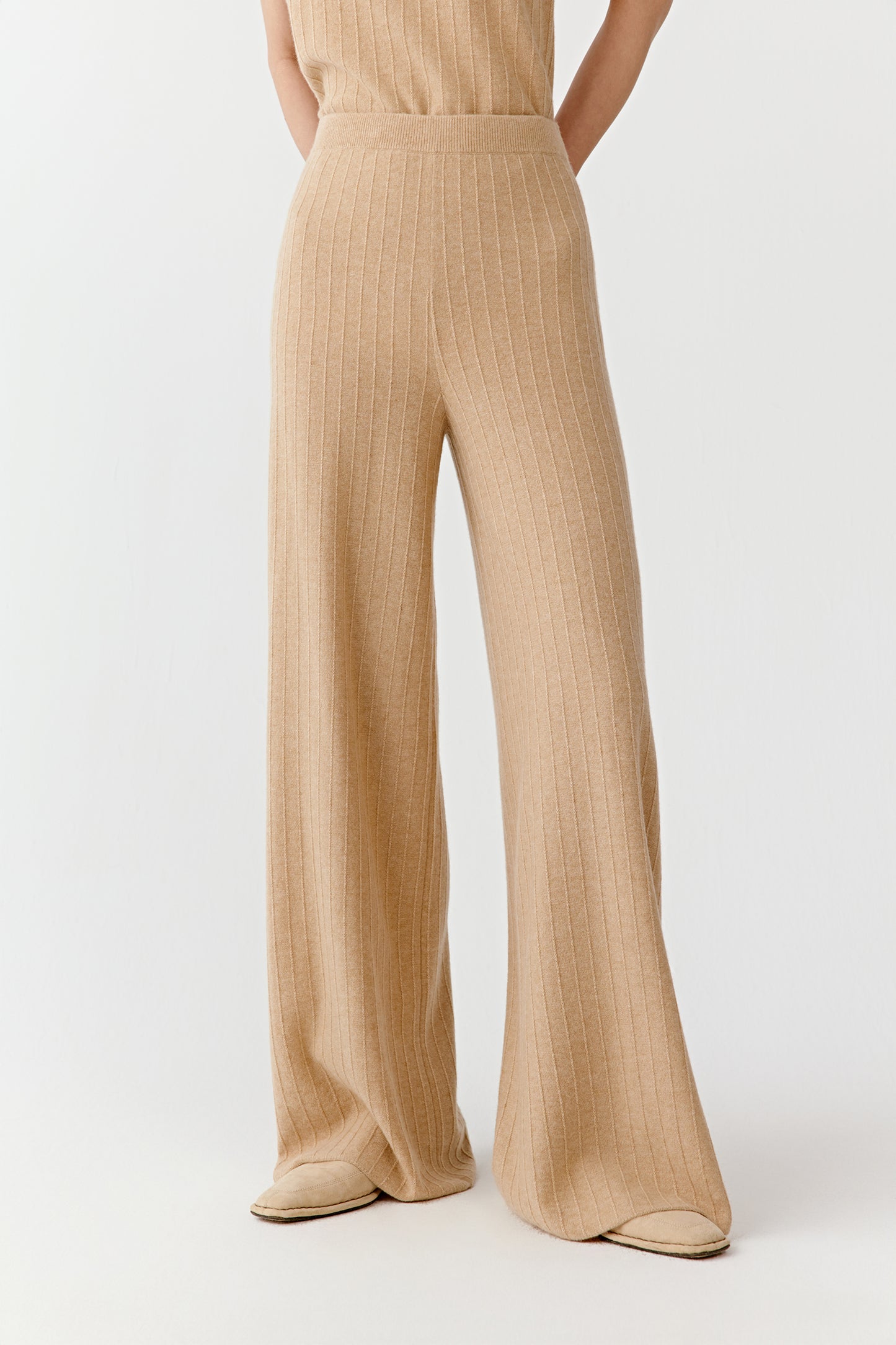 Full view of beige wide leg knit pants styled with a sleeveless beige top on a light background