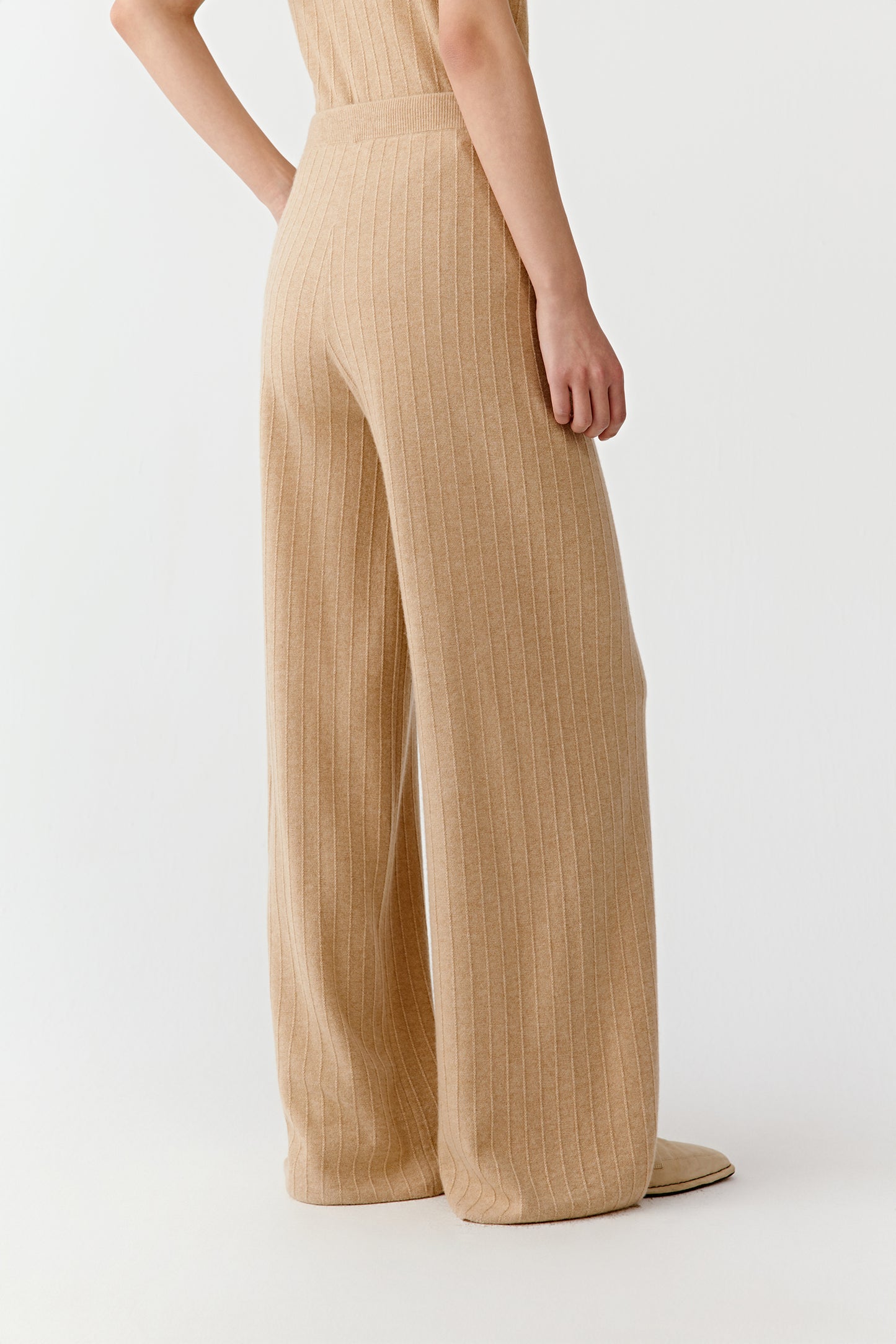 Side view of a sleeveless beige knit top and wide leg trousers on a light background