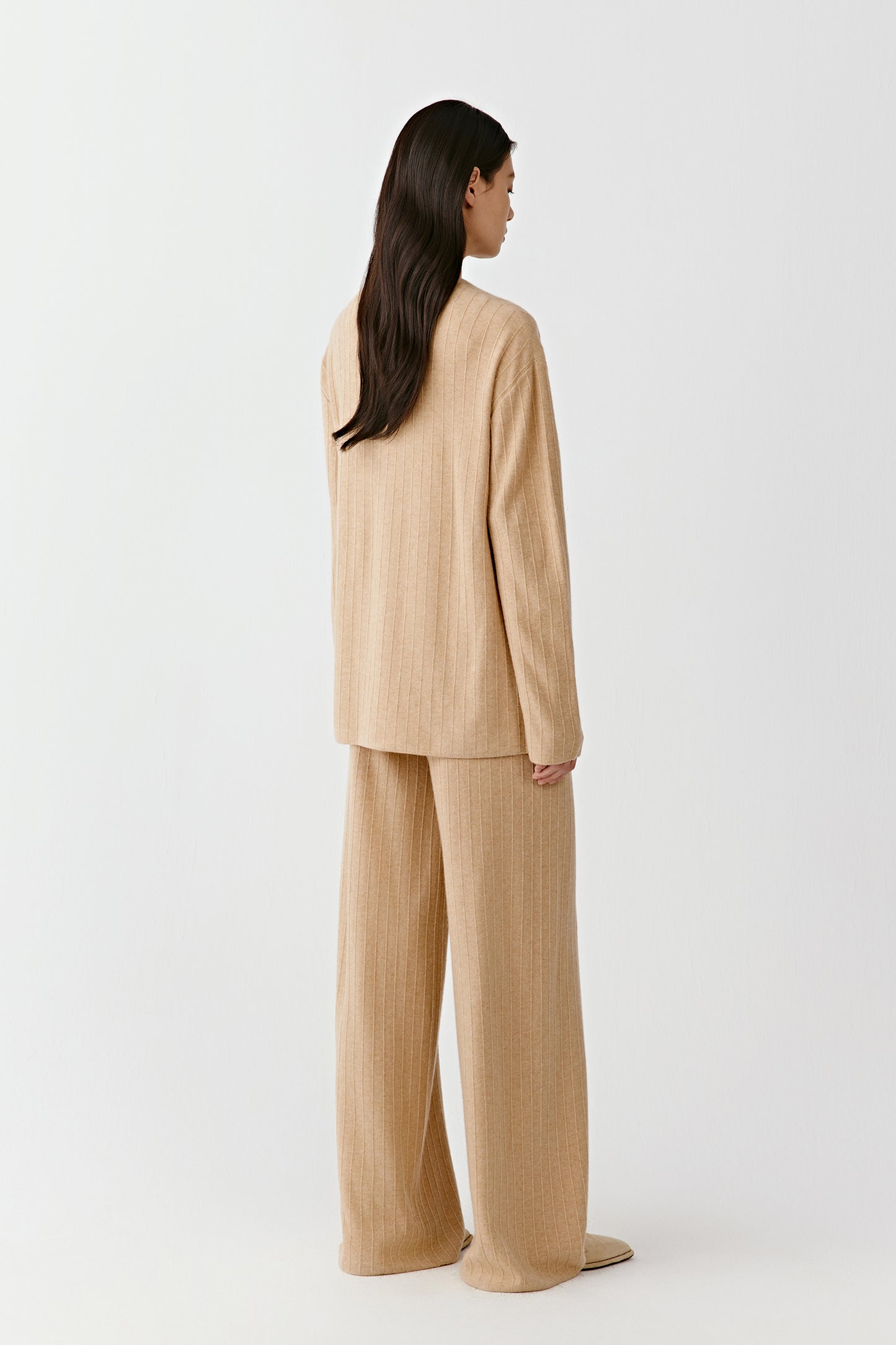 Back view of a beige knit cardigan and matching trousers on a light background