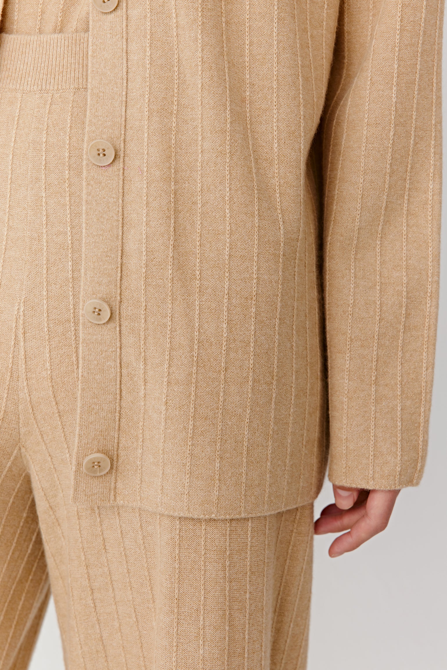 Detail of a beige knit cardigan sleeve and pocket on a light background