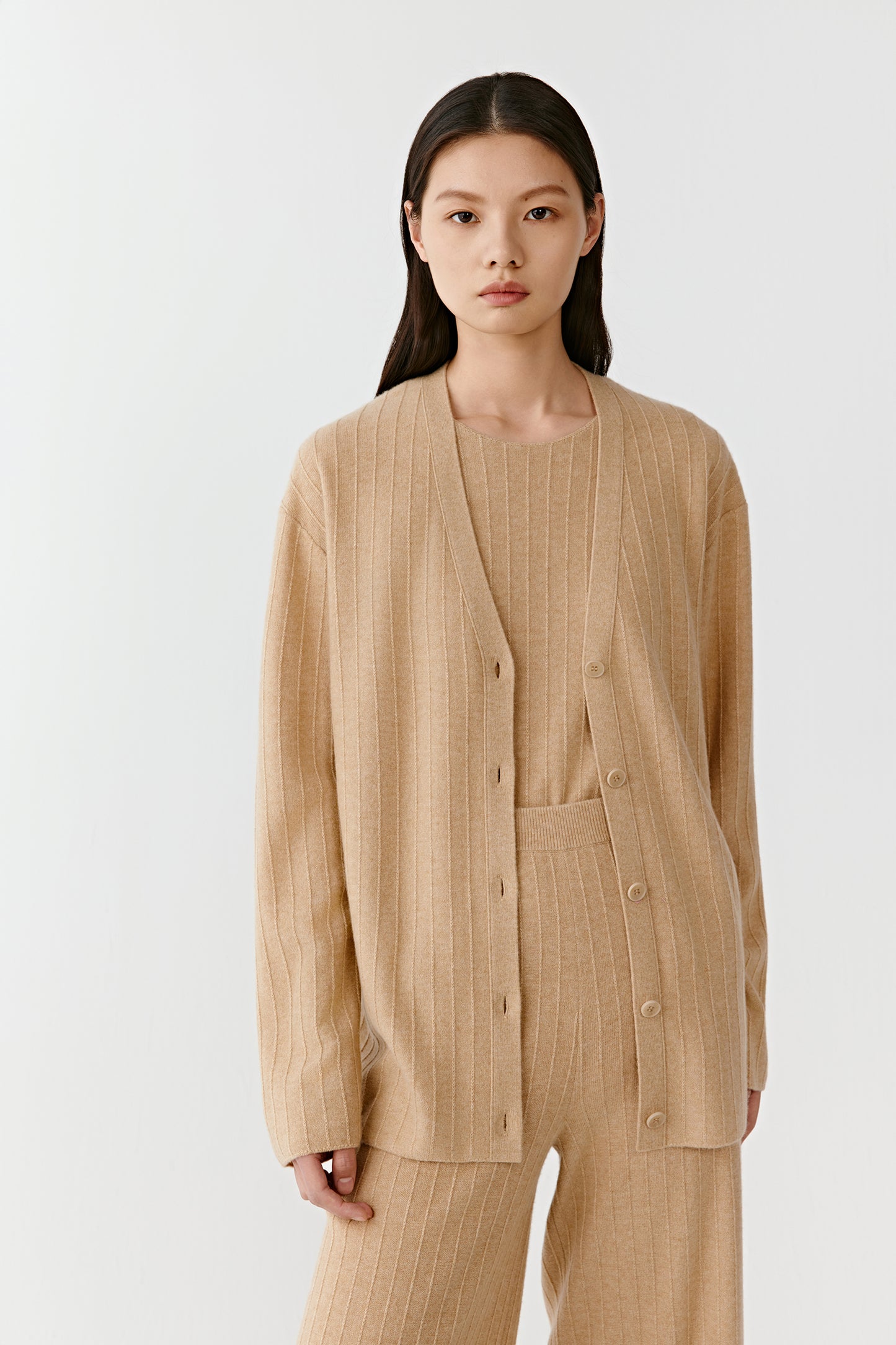 Woman wearing a beige knit cardigan with front buttons styled with matching knit pants on a light background