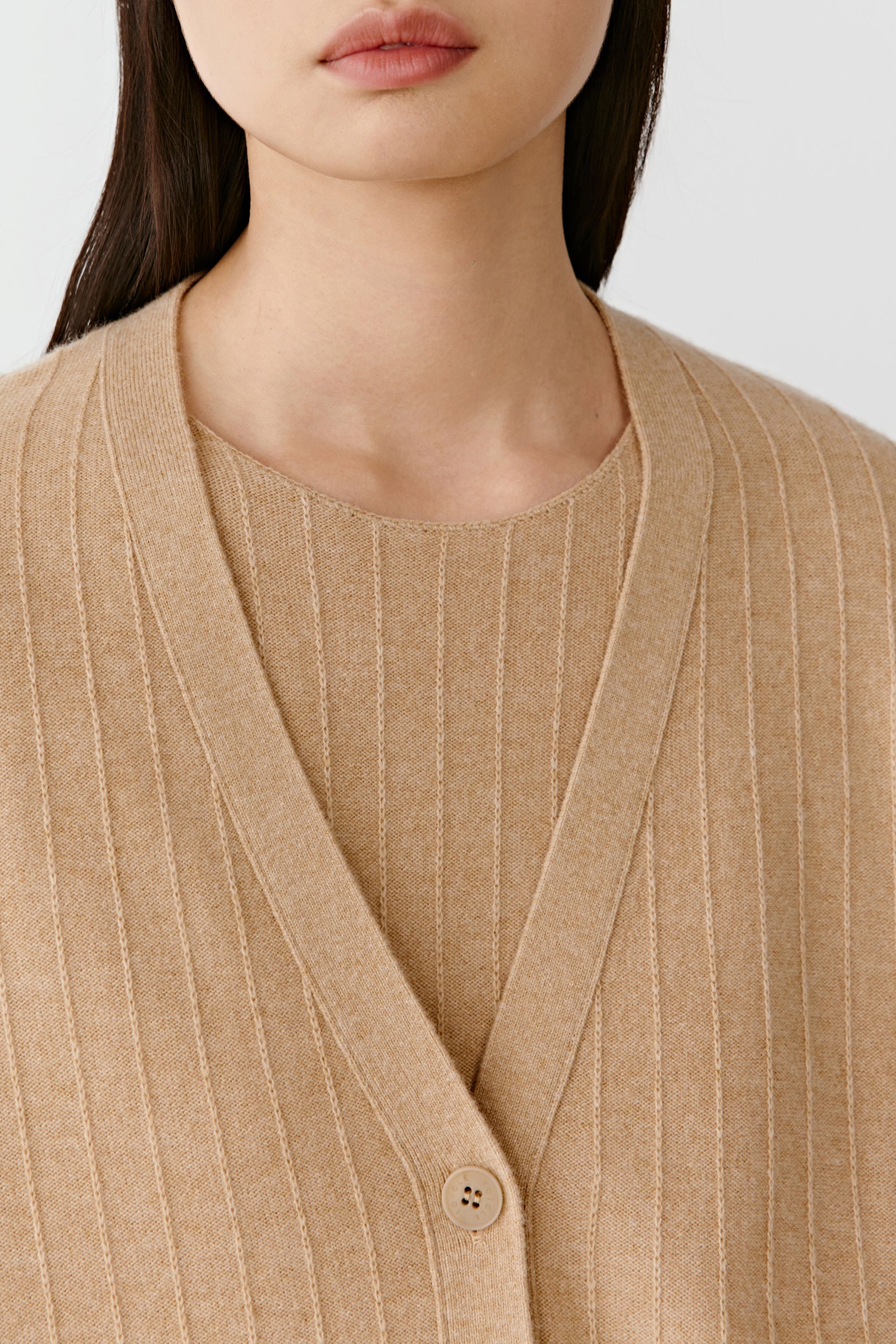 Close-up of a beige knit cardigan neckline and buttons on a light background
