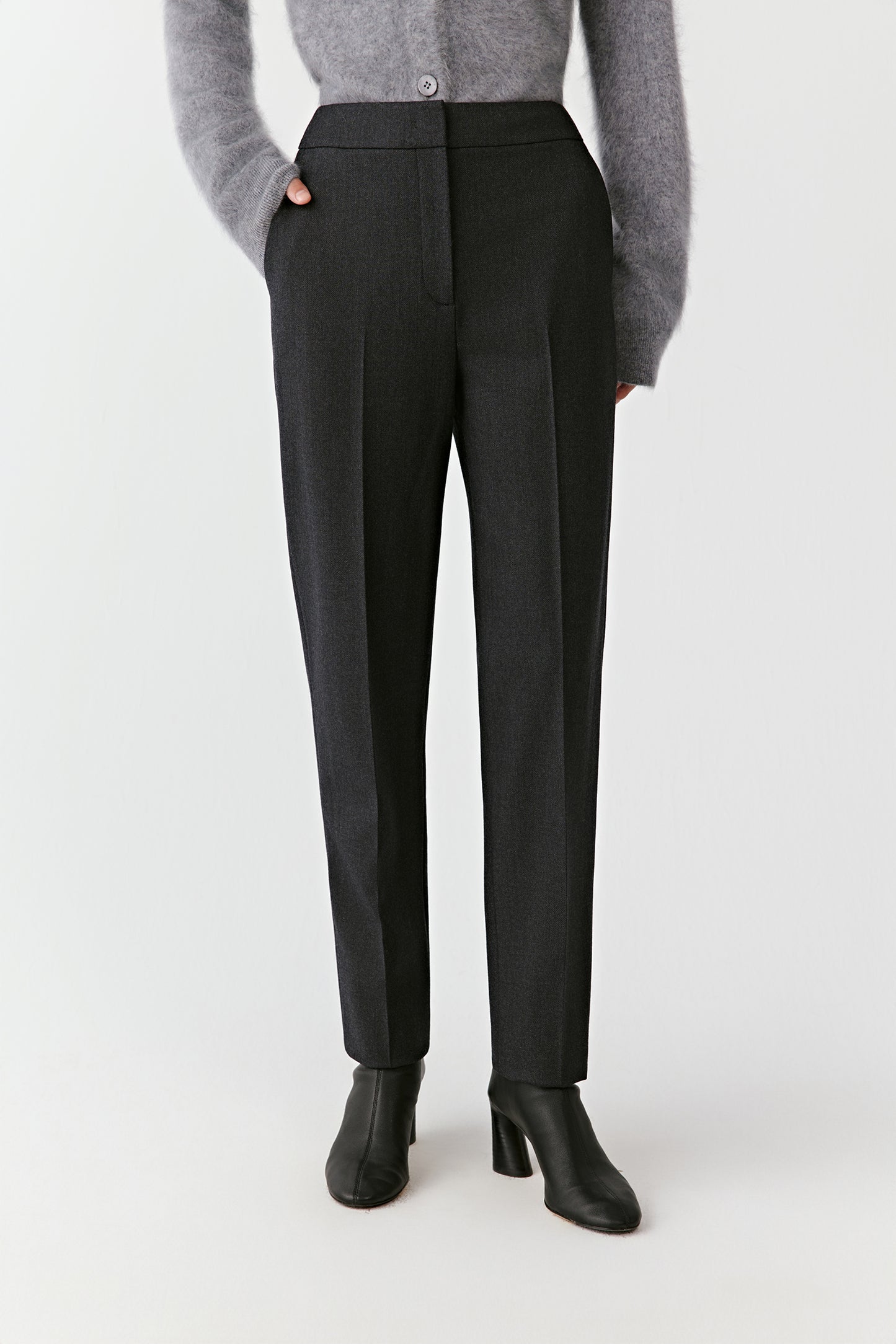 Front-facing view of black tailored trousers and a gray sweater, showing clean lines and a minimalist silhouette.
