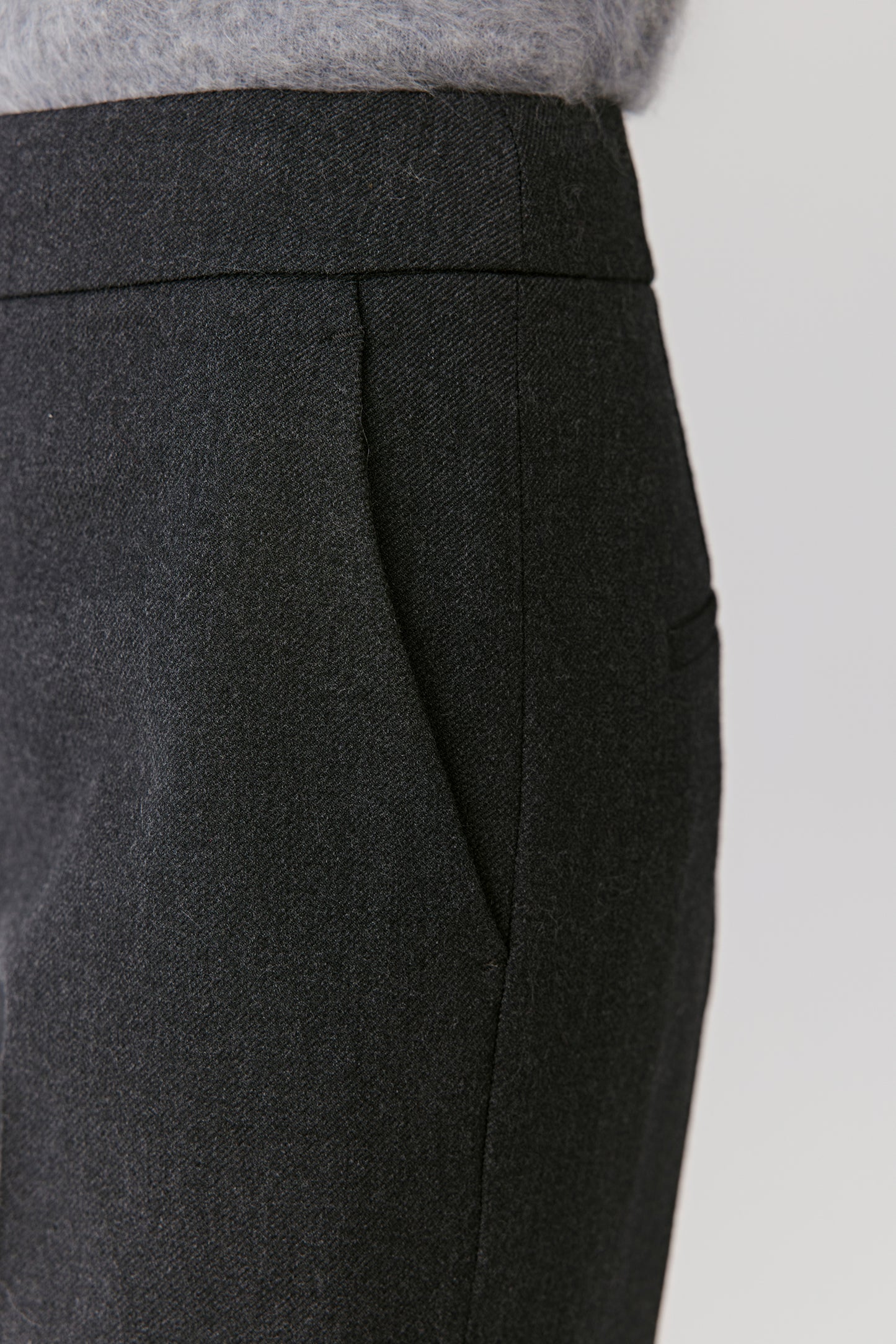 Detail view of the waistband and front pleats of the black tailored trousers.