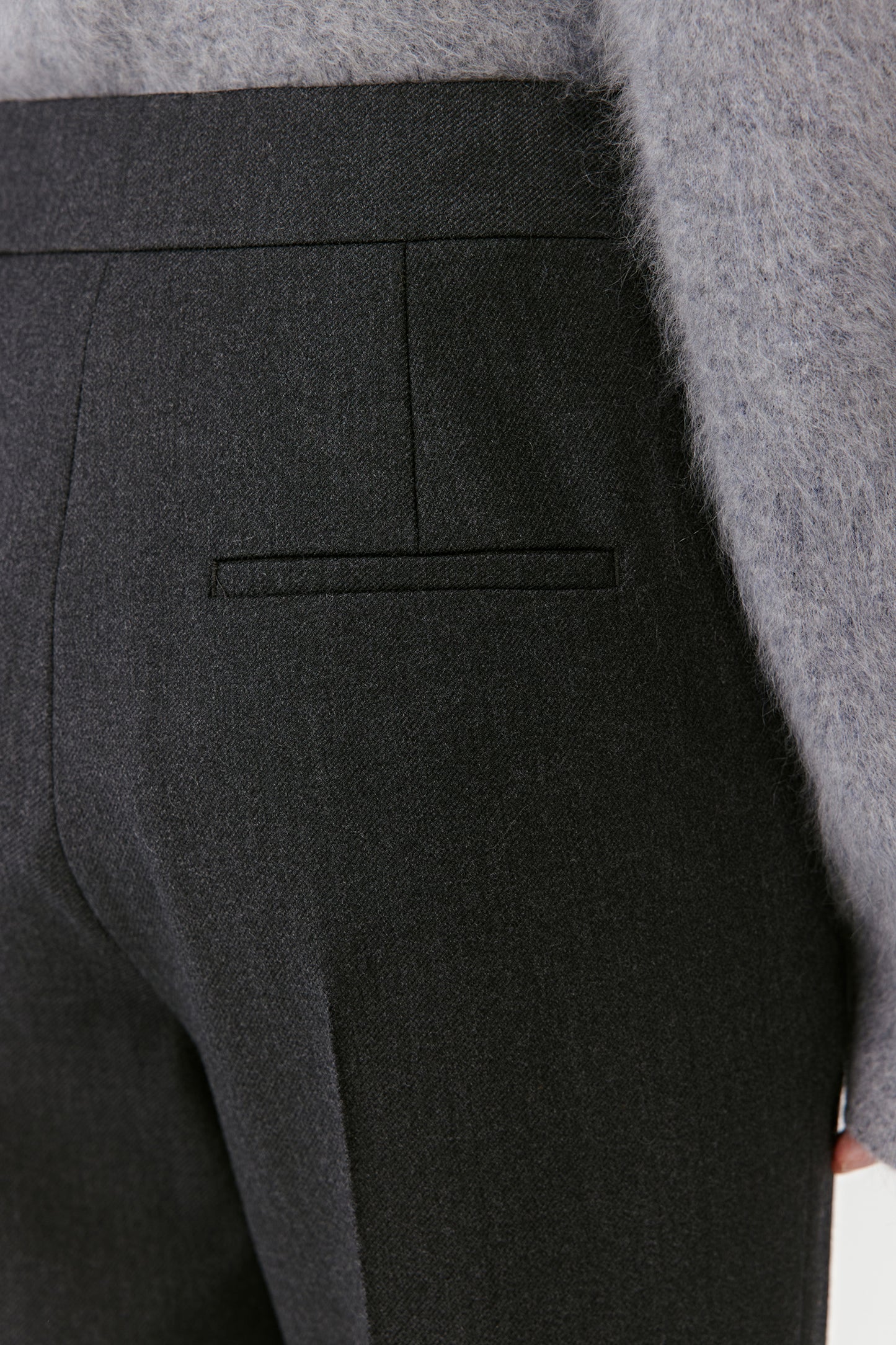 Close-up on the back of the black trousers showing welt pockets and smooth fabric finish.