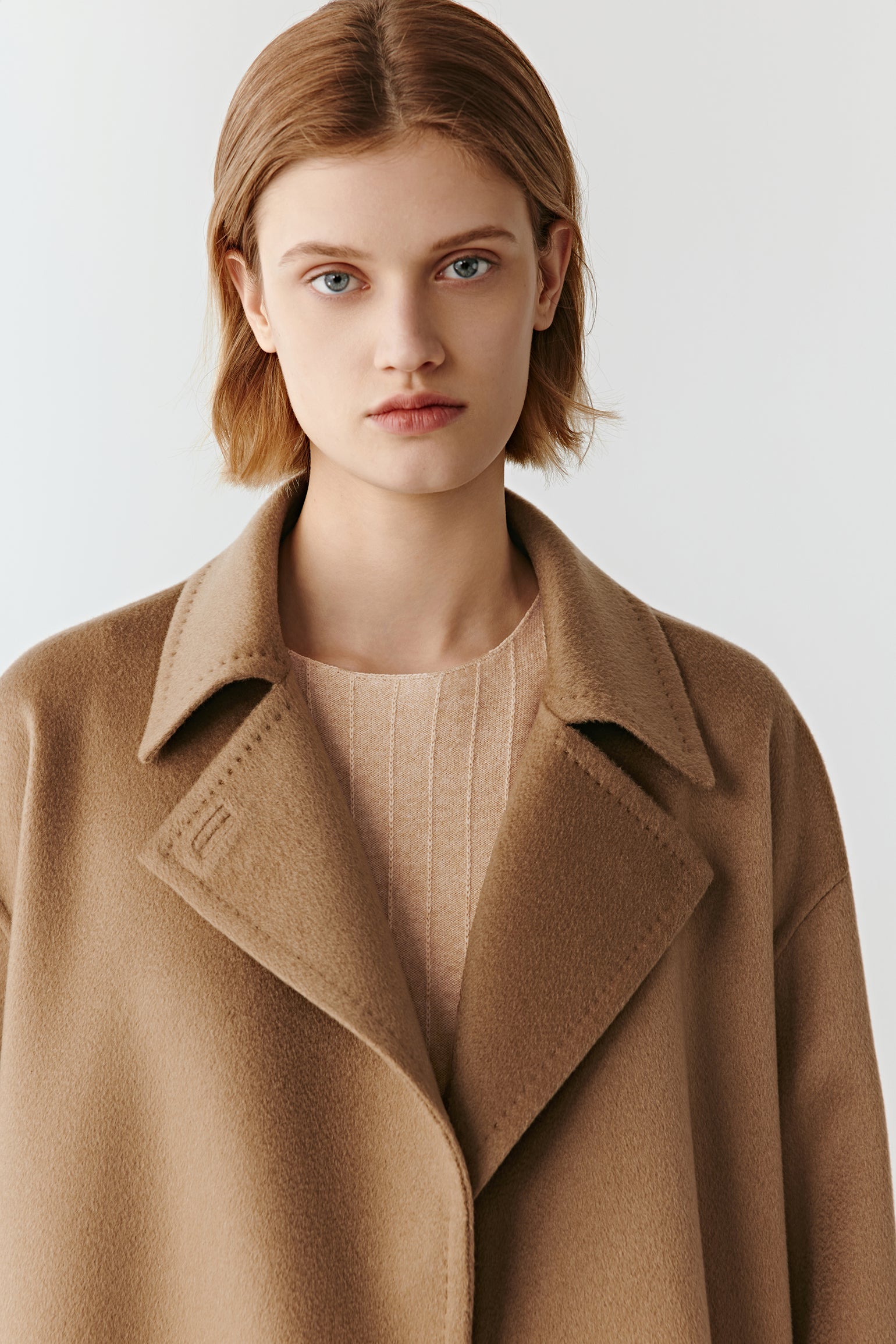 Close-up of a camel belted jacket collar and lapel detail on a light background