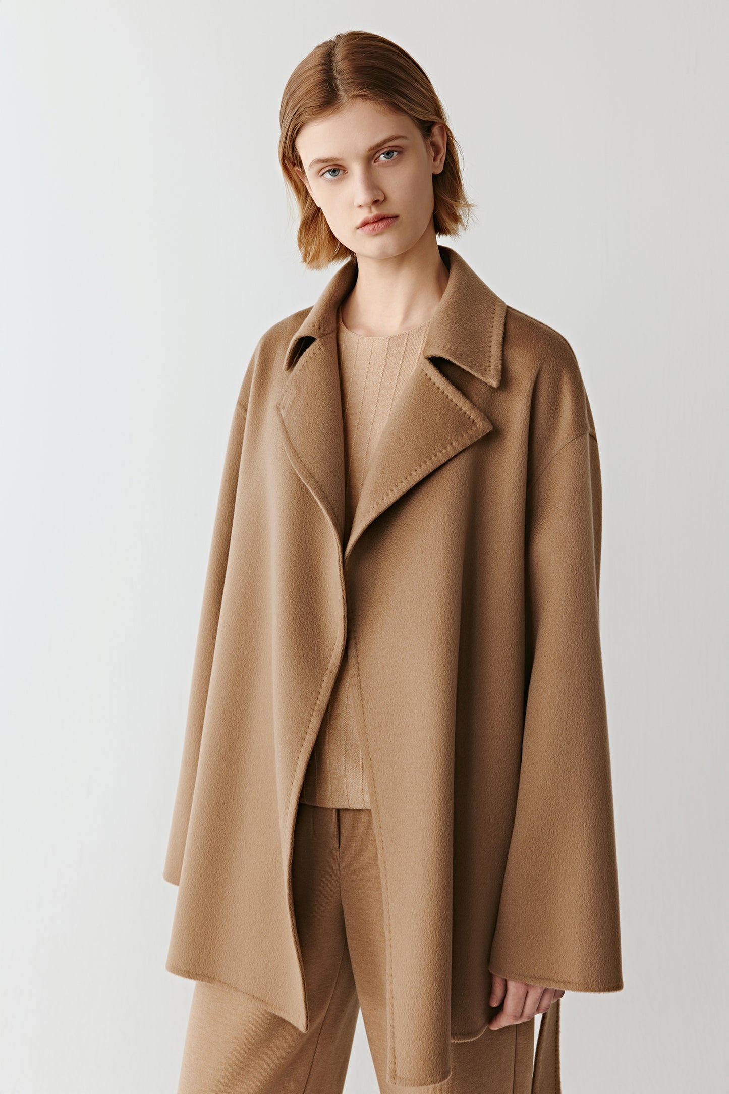 Front view of a camel wool belted jacket with wide lapels on a light background