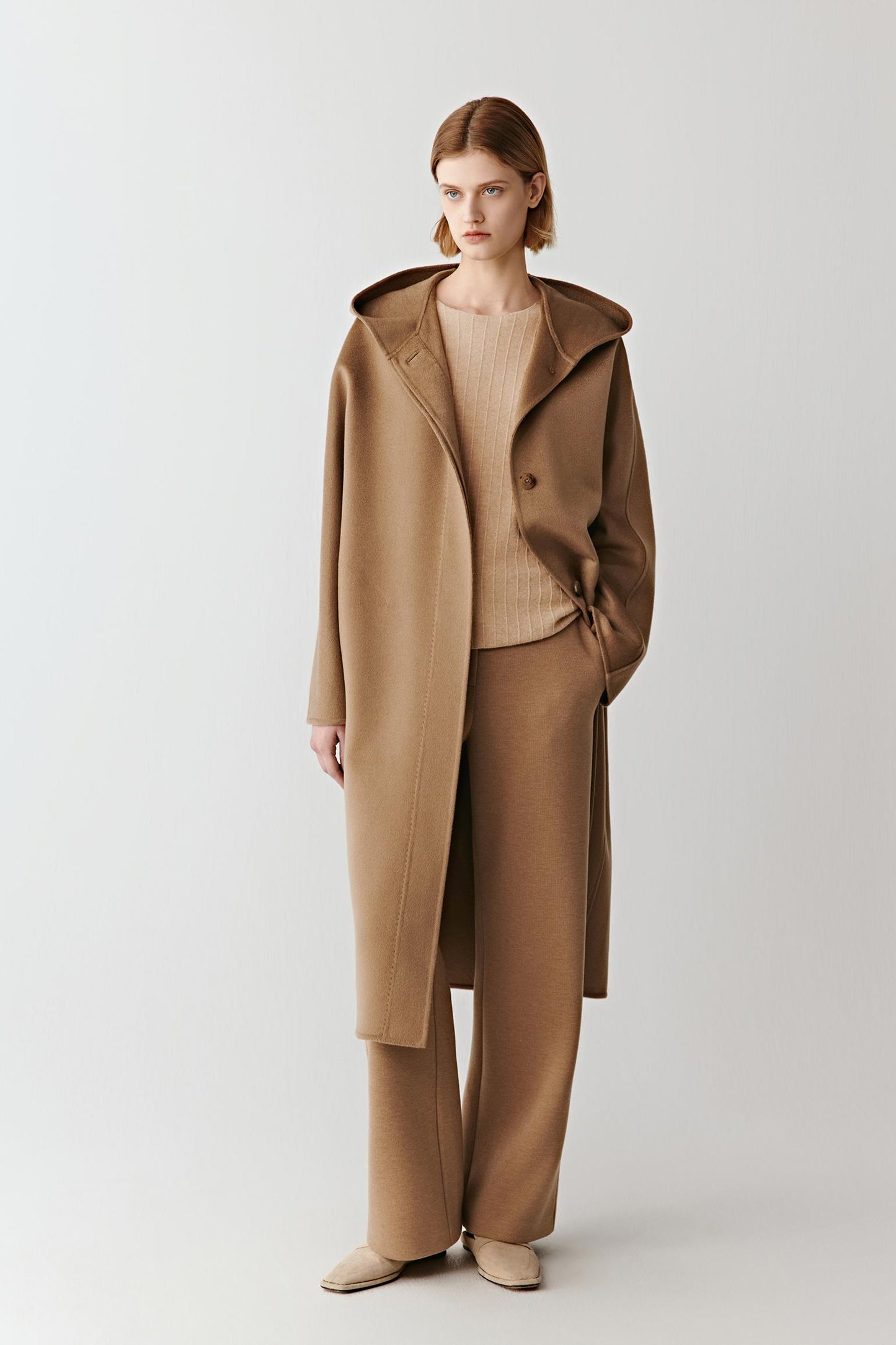 Model wearing a camel wool coat over matching wide-leg trousers and a beige top, standing against a plain background.