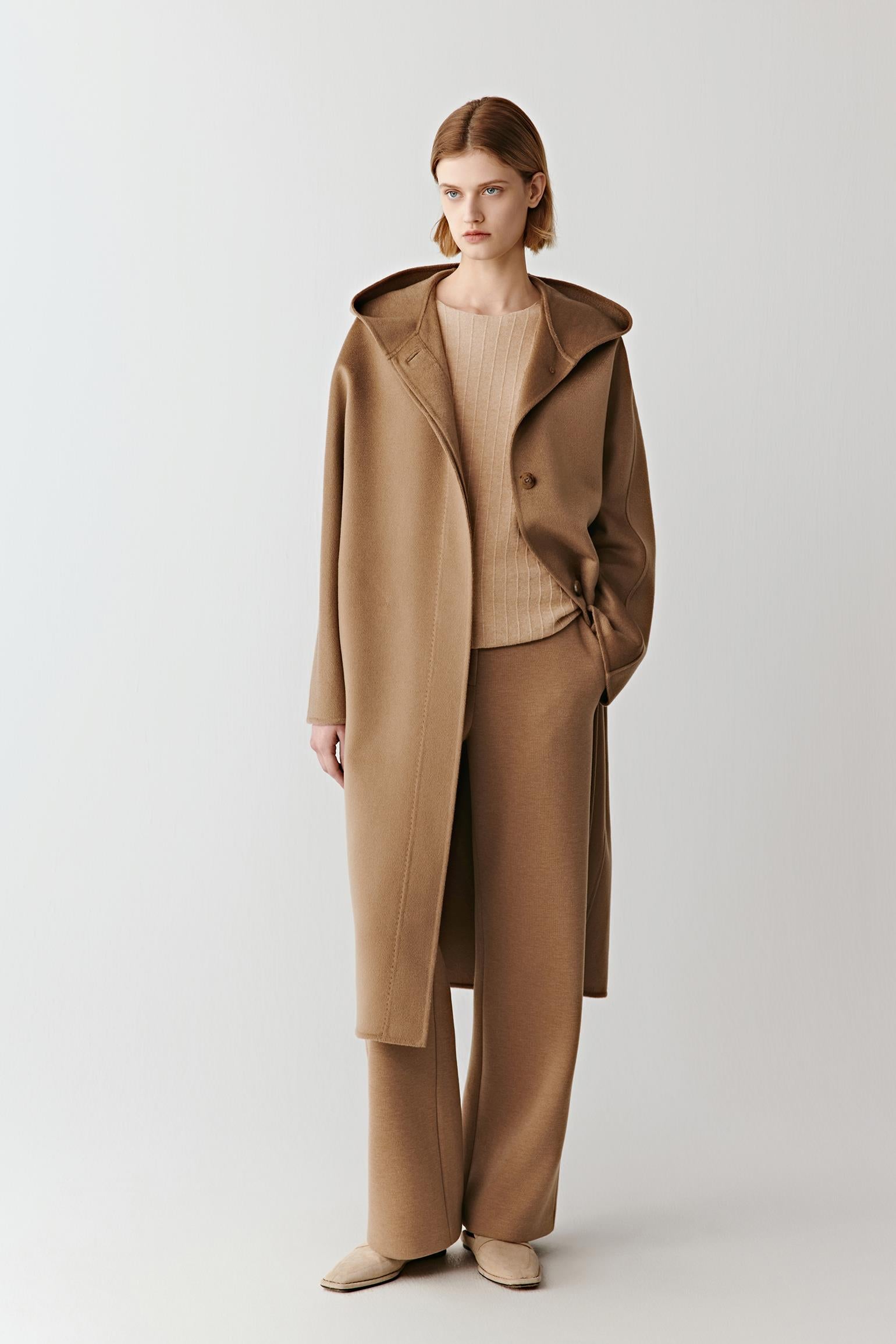 Model wearing a camel wool coat over matching wide-leg trousers and a beige top, standing against a plain background.