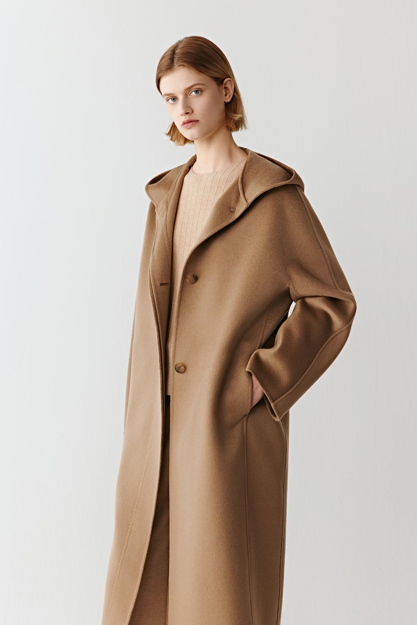 Profile view of the camel coat showing its long straight cut, large lapel, and relaxed oversized silhouette.