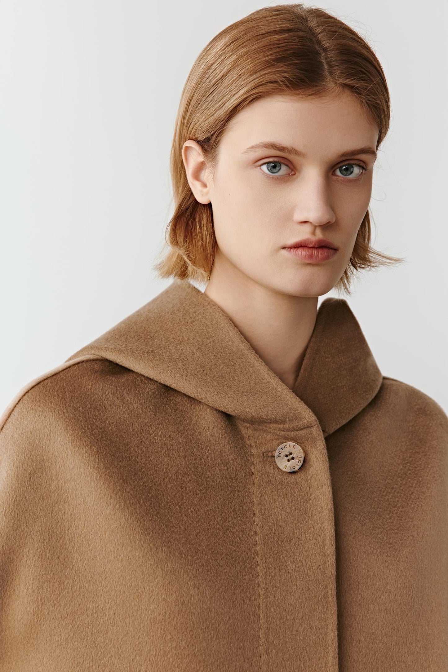 Close-up of the camel coat’s collar and single button closure, showing wool texture and refined finish.