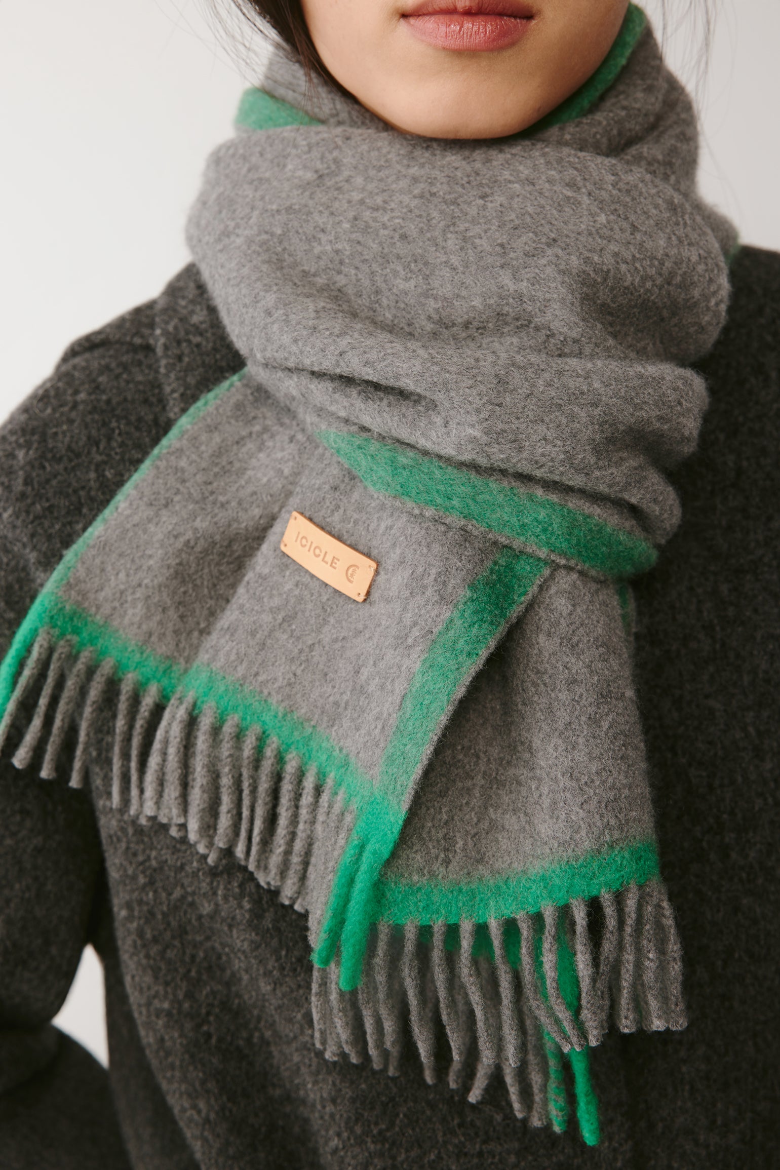 Close-up of a grey wool scarf with green edge detail on a dark coat