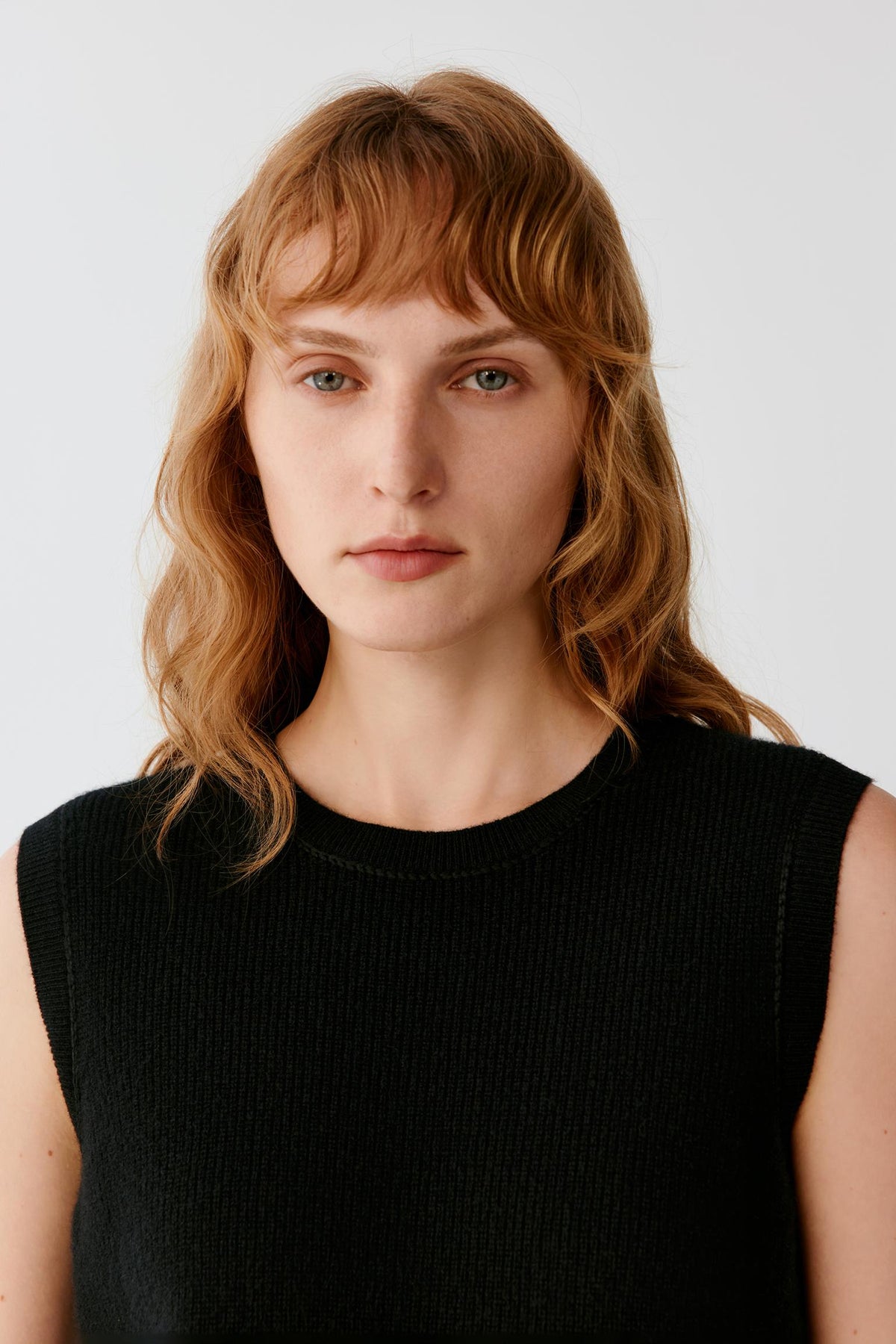 Close-up highlighting the round neckline, wide armholes and fine black cashmere knit.