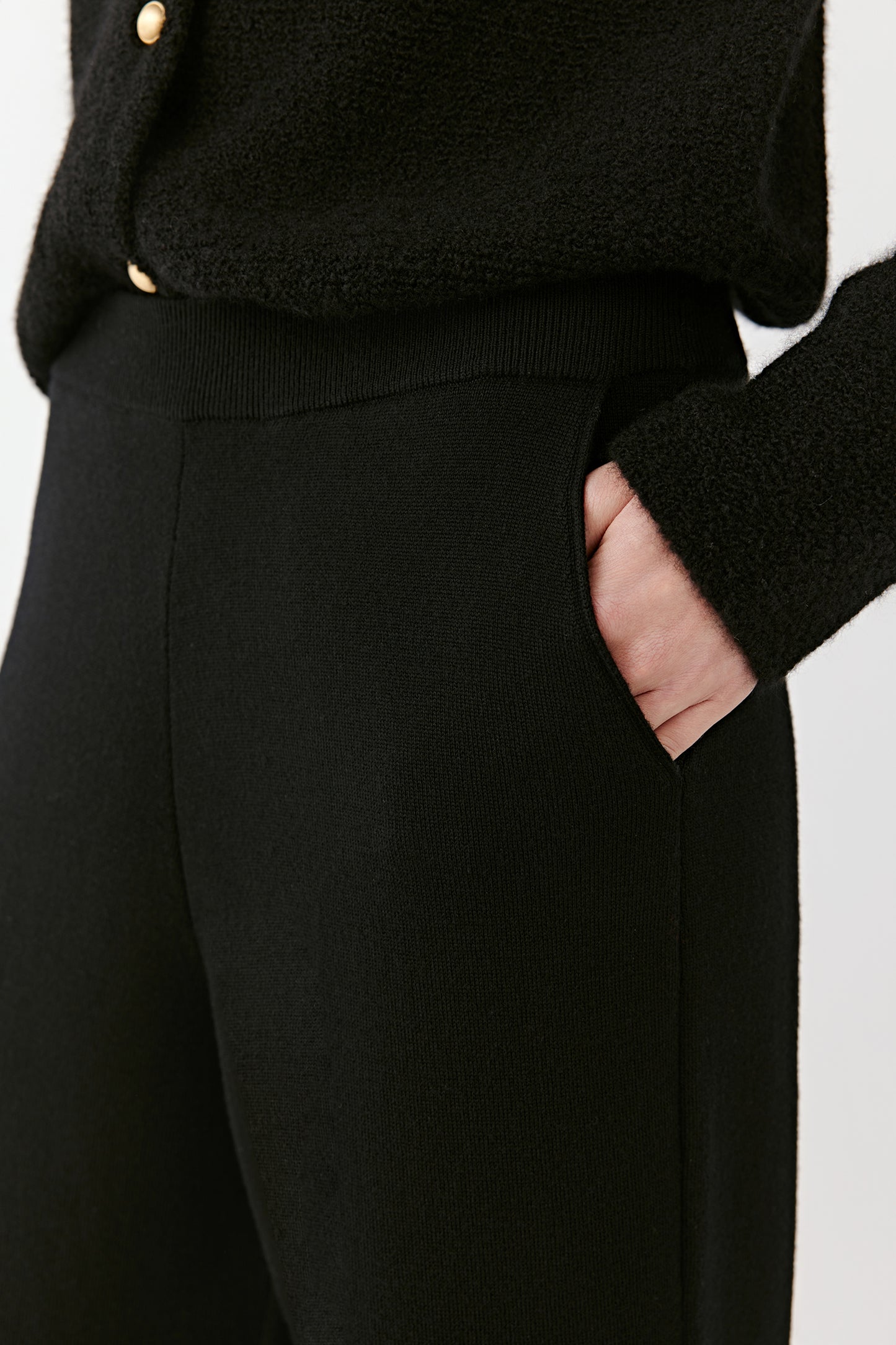 Close-up of the upper section of black wide-leg merino wool trousers, focusing on the waistband, pocket detail, and soft dense weave.