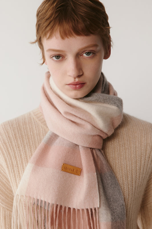 A close-up of a woman wearing a pink checked cashmere scarf, showing the soft texture and pastel tones.