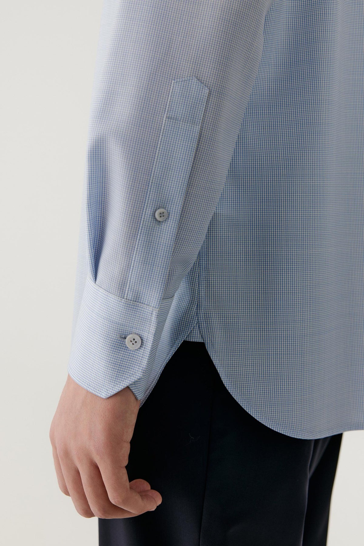 Close-up of the long sleeve and buttoned cuff of the light blue checked worsted wool shirt.