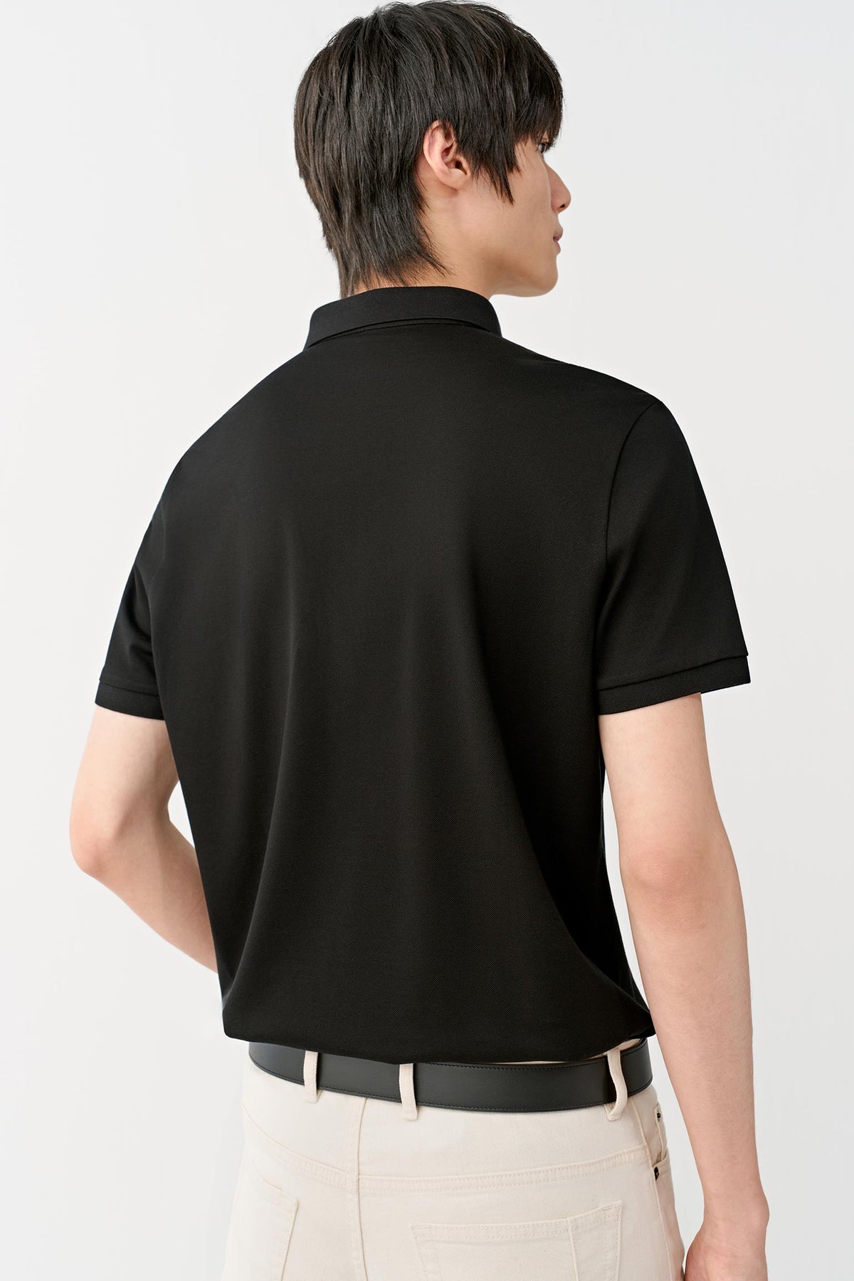 A man shown from the back wearing a black short-sleeve polo shirt and light beige trousers, photographed against a clean white studio background.