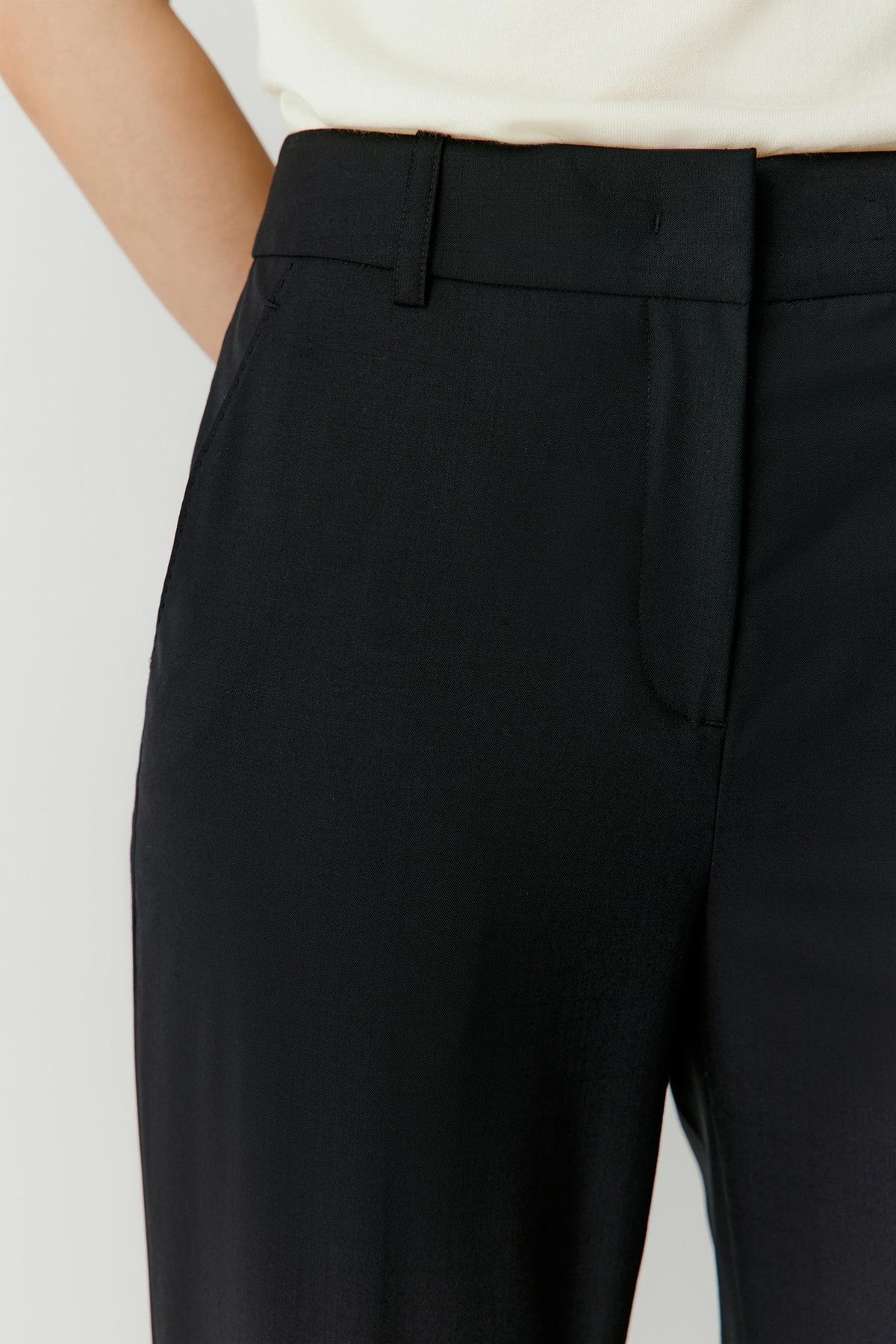 Close-up of the mid-rise waist and concealed front fastening of the black worsted wool trousers.