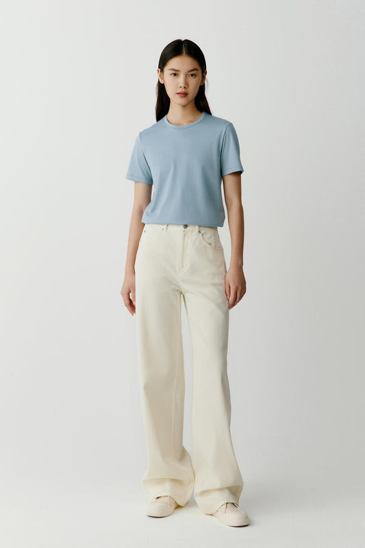 Full-length front view showing the T-shirt styled with off-white trousers. The straight cut, round neckline and short sleeves create balanced proportions, while the lightweight cotton jersey drapes softly and follows the body with ease.
