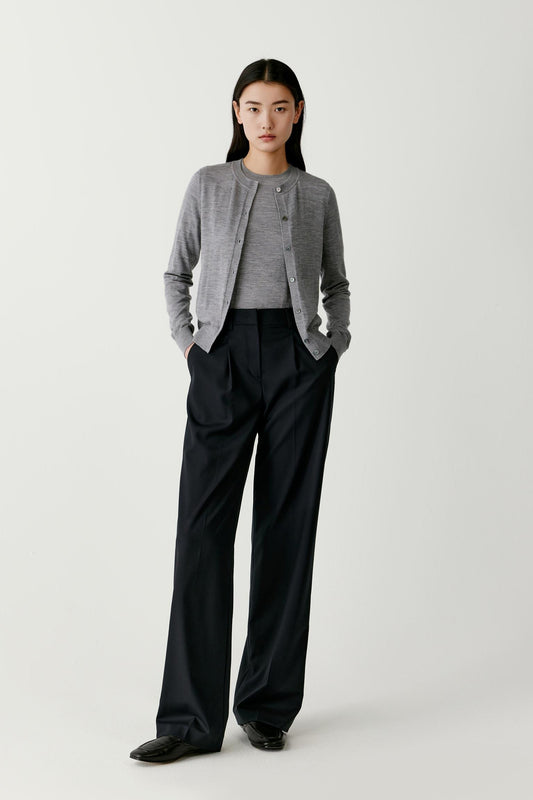 Full-length front view showing the overall silhouette of the grey wool cardigan worn with black trousers. The cardigan has a clean minimalist structure with a straight hem and a relaxed fit through the shoulders and torso. The button placket runs vertically along the center front, emphasizing the balanced proportions of the garment.