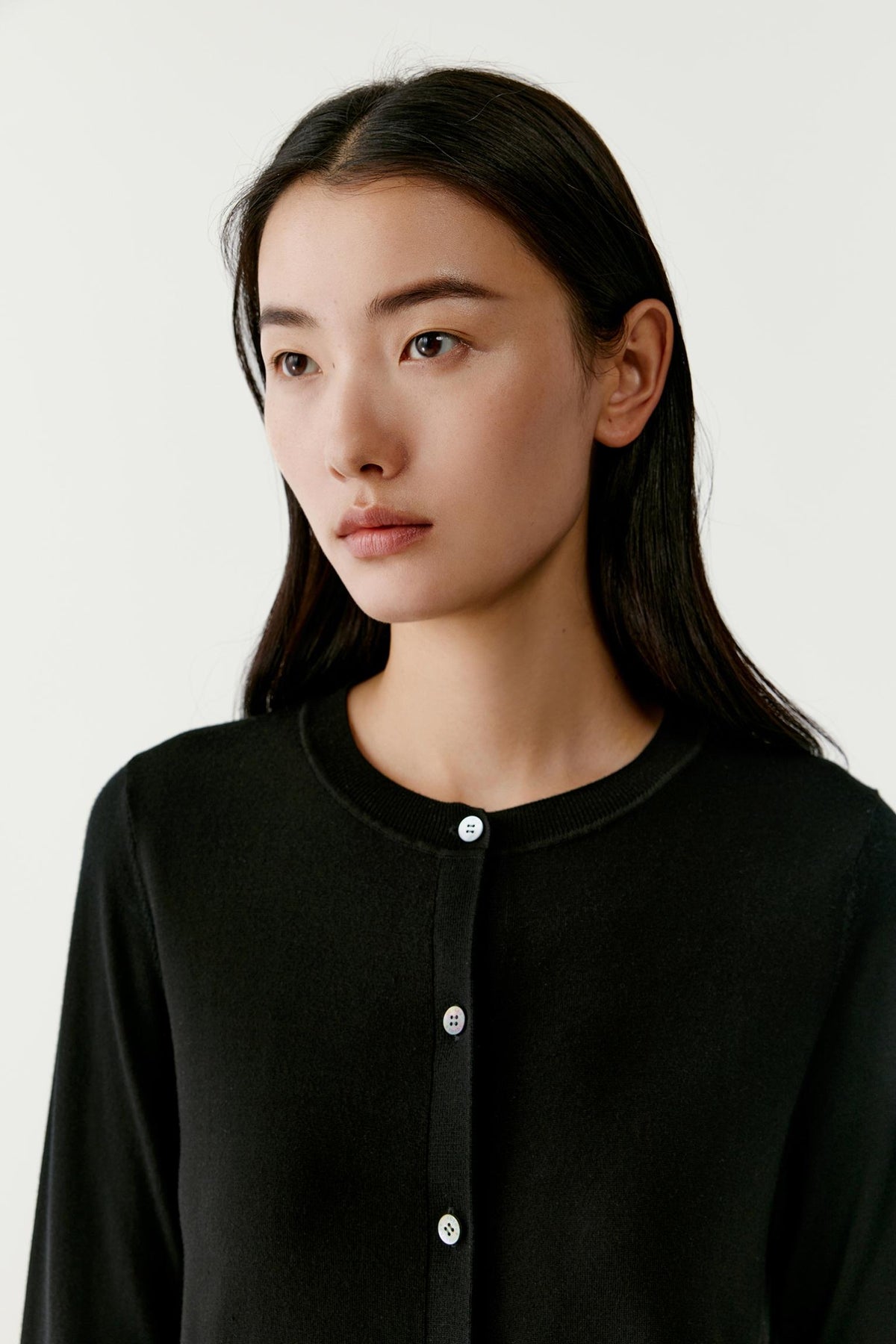 Close-up of the deep black wool cardigan, highlighting the round neckline and button-front fastening.