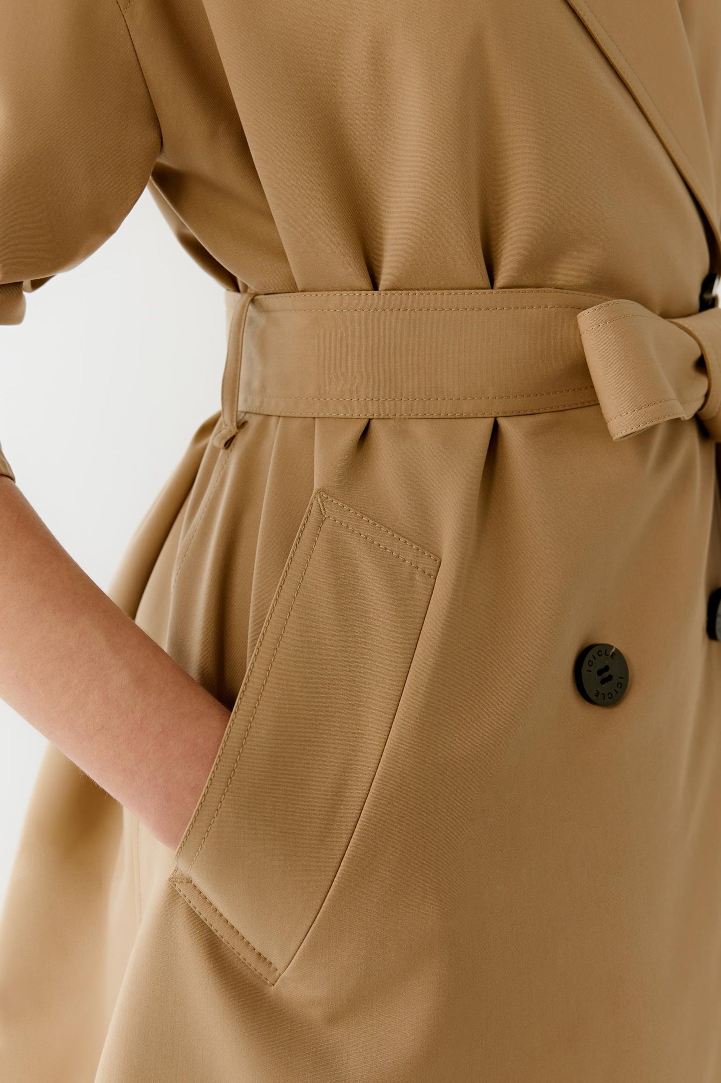 Close-up view focusing on the side waist construction and gathered belt area. The image highlights the clean seam lines, soft drape of the fabric and refined tailoring details that contribute to the balanced silhouette of the trench coat.