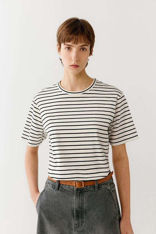 Portrait view focusing on the upper body, showcasing the round neckline, shoulder construction and striped pattern. The fine jersey knit reveals a smooth, even surface with soft texture and subtle depth created by the alternating cream and black stripes.