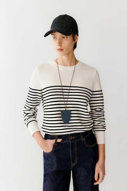 Front view portrait of a woman wearing a navy silk and cotton knit sleeveless top, paired with light ivory trousers, highlighting the fitted silhouette, clean armholes and the vertical openwork knit structure with a subtly textured surface