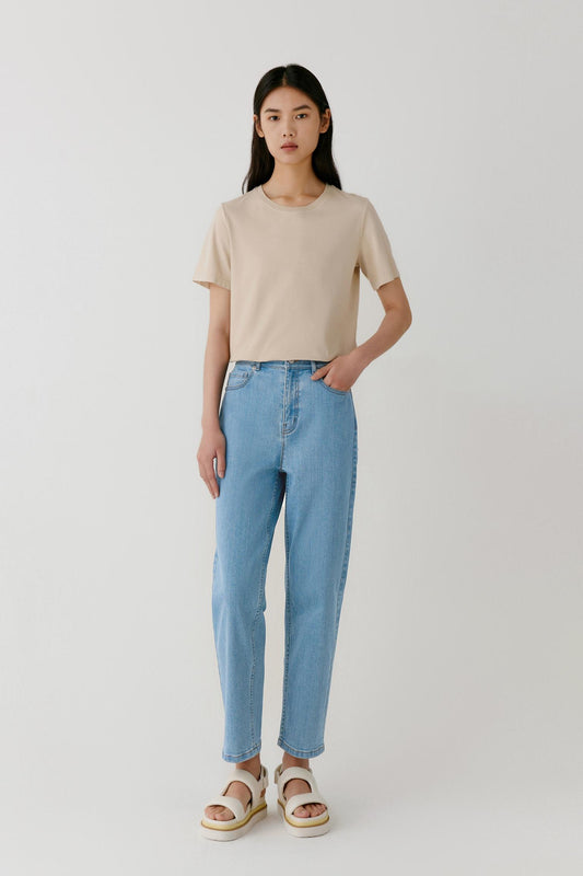 Full-length front view showing the balanced proportions of the T-shirt paired with blue denim trousers. The image emphasizes the fluid drape of the lightweight cotton jersey and the understated simplicity of the silhouette.