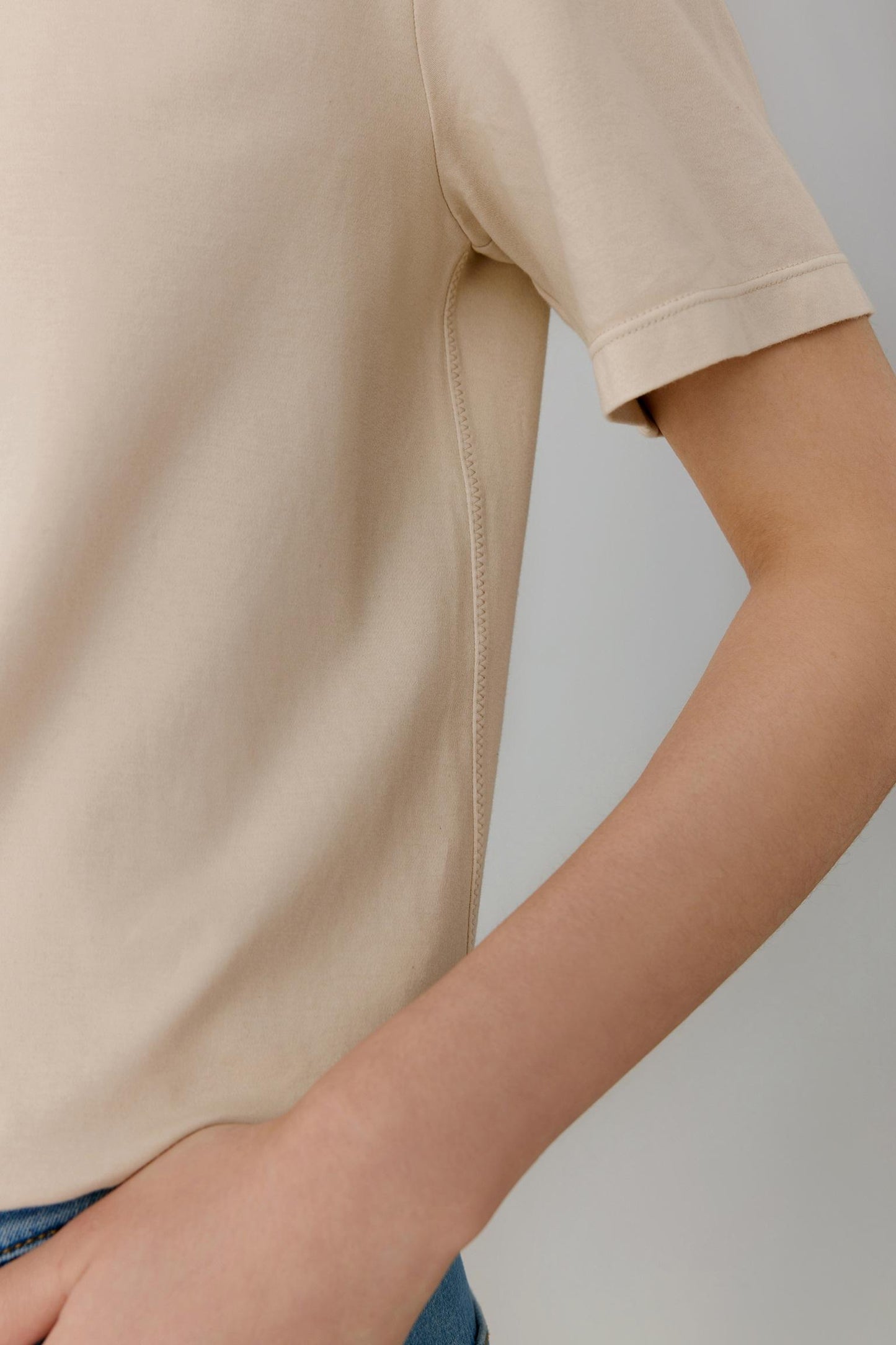 Close-up view of the sleeve and side body area. The image highlights the lightweight jersey structure, smooth surface and soft drape of the fabric, while showcasing the clean finishing and subtle tonal depth of the beige shade.