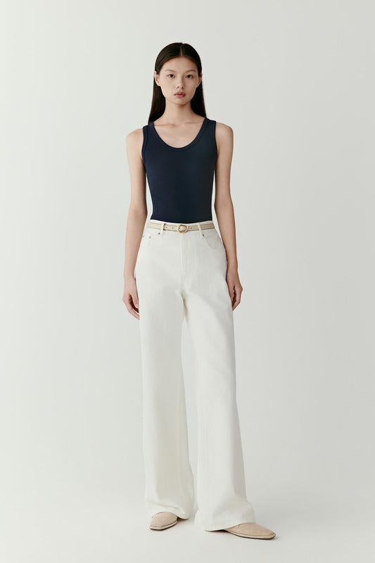 Full-length front view showing the fitted silhouette of the navy rib jersey tank top worn with off-white straight-leg trousers. The ribbed texture creates subtle vertical lines that enhance the close-fitting shape.