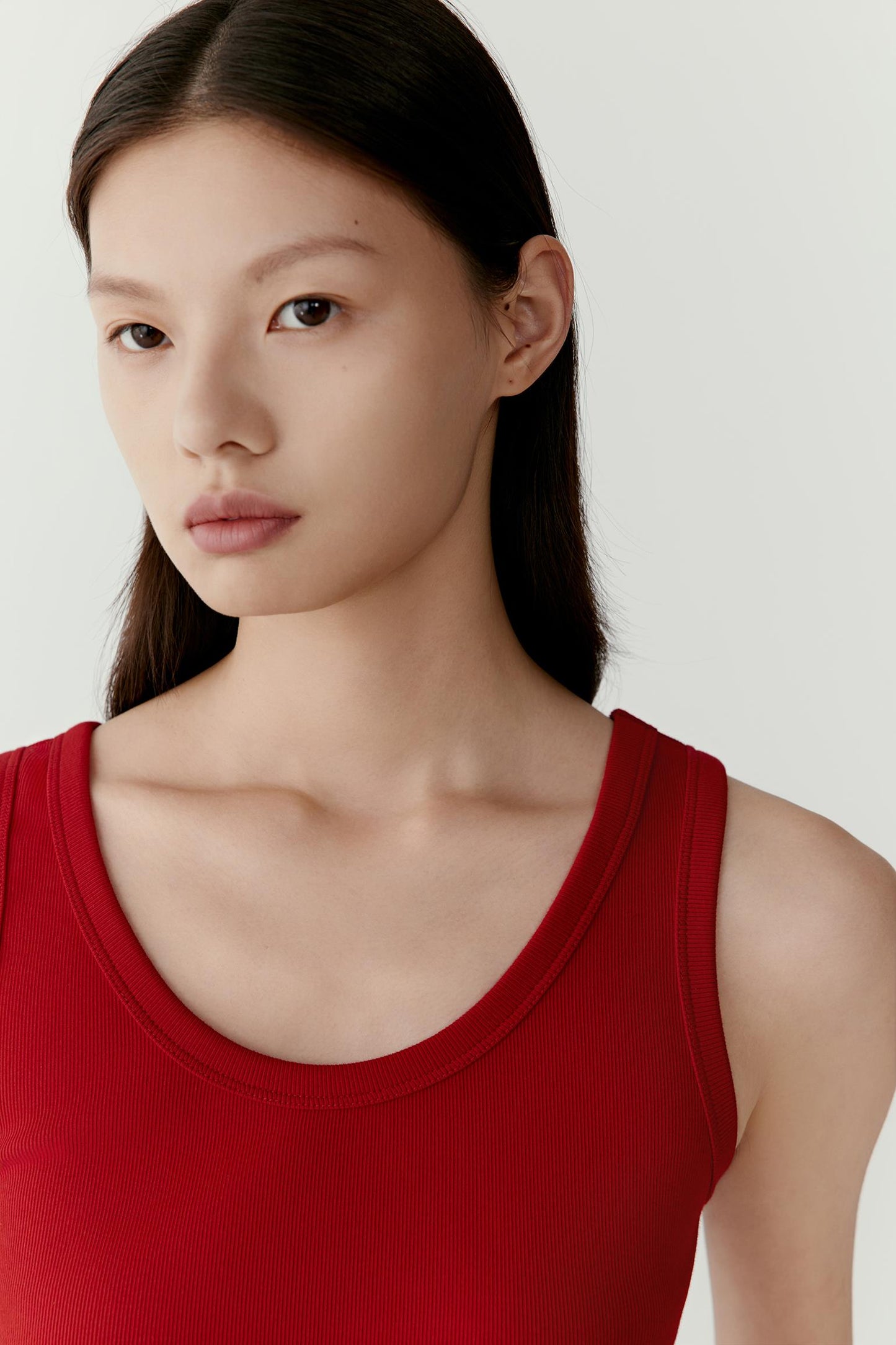 Close-up portrait focusing on the scoop neckline, shoulder line and upper body construction. The image highlights the fine rib texture, soft matte surface and even knit structure, while showcasing the saturated deep red shade and minimal detailing.
