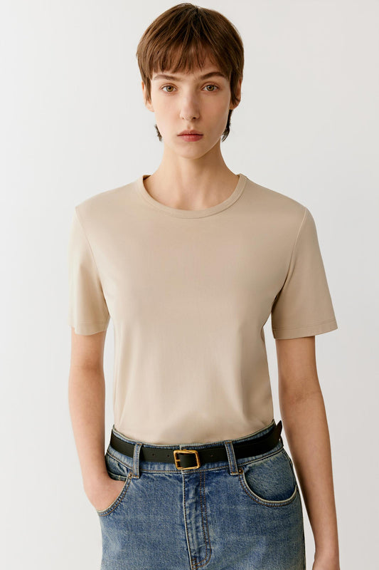 Front view of a woman wearing a beige cotton jersey T-shirt, highlighting the smooth jersey surface, soft hand and lightweight construction. The clean design and neutral tone emphasize the simplicity of the silhouette, while the fabric falls naturally with a fluid drape.