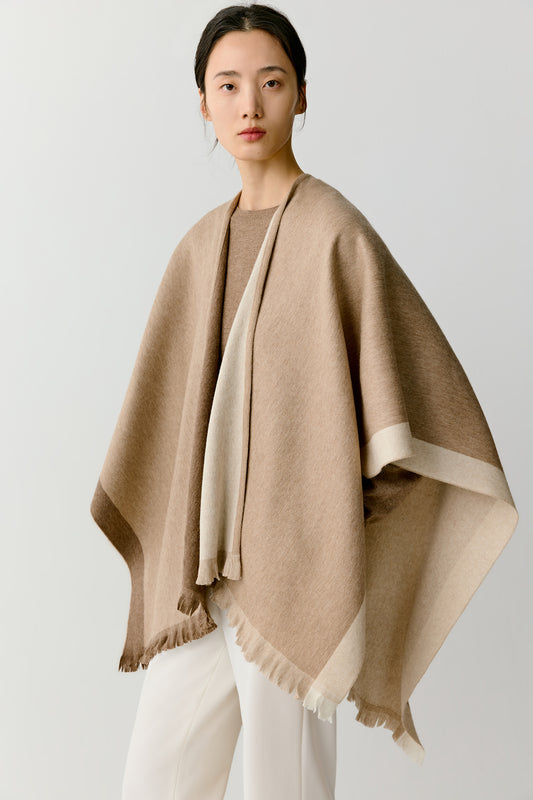 Full-length view of a woman wearing an undyed cashmere shawl in natural tones, draped softly over a beige outfit.
