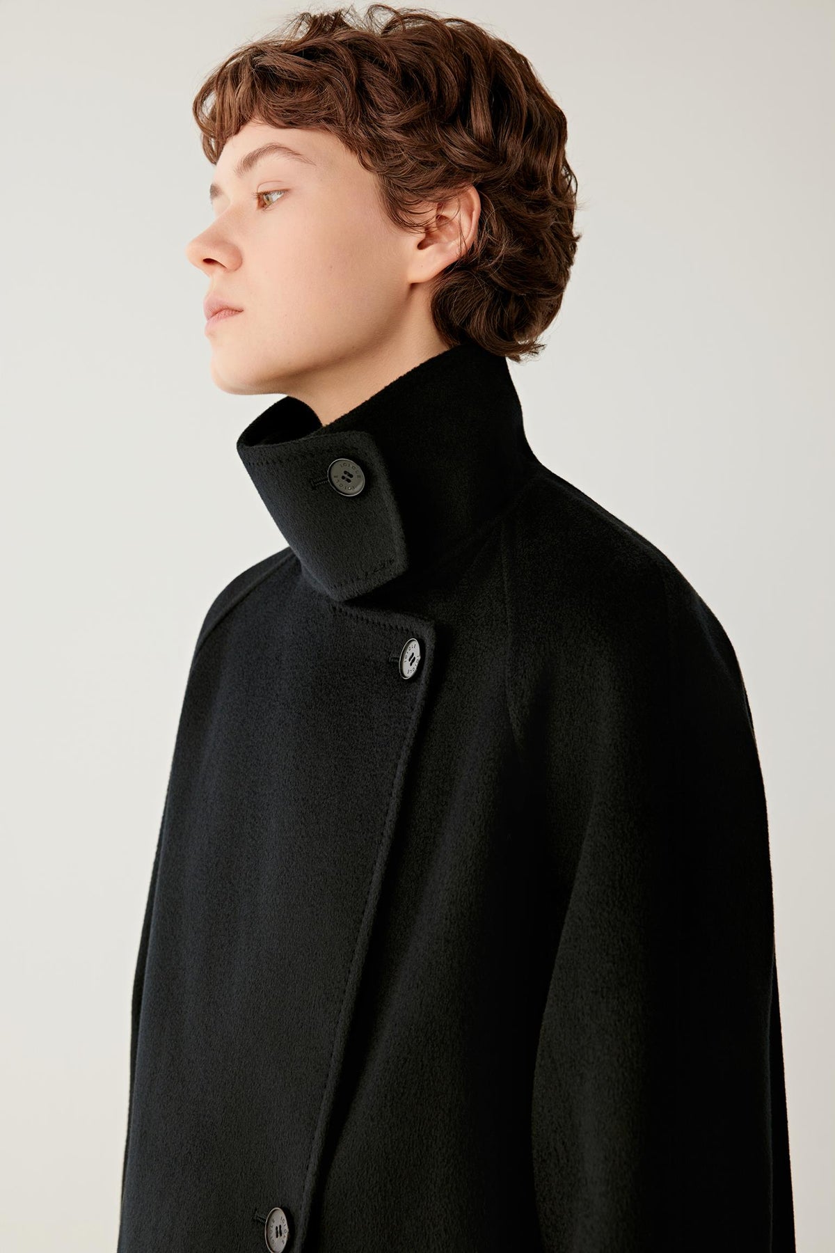 Close-up highlighting the high stand collar, asymmetric button fastening and soft deep black cashmere surface.