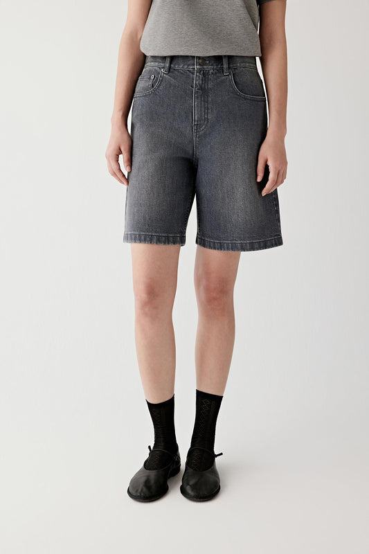 Three-quarter view showing the relaxed proportions of the shorts and the structured fall of the denim fabric from the waist to the hem.