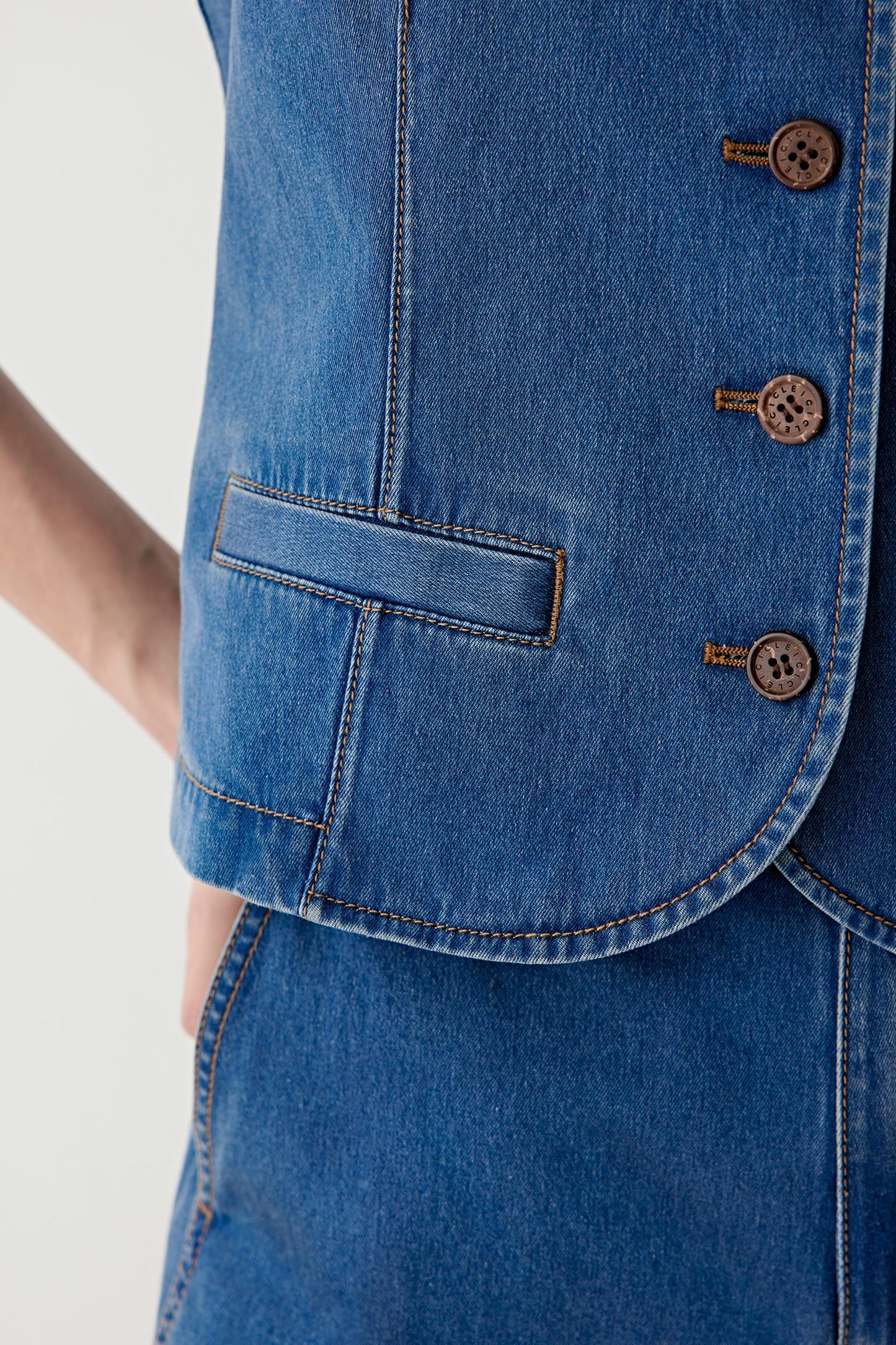 Close-up of the front button placket and hem, highlighting the contrast stitching, metal buttons and precise finishing of the denim fabric.