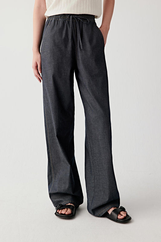 Mid-length front view focusing on the trousers from waist to hem, emphasizing the wide-leg cut, the vertical fall of the fabric and the slightly textured woven denim surface in a deep navy shade
