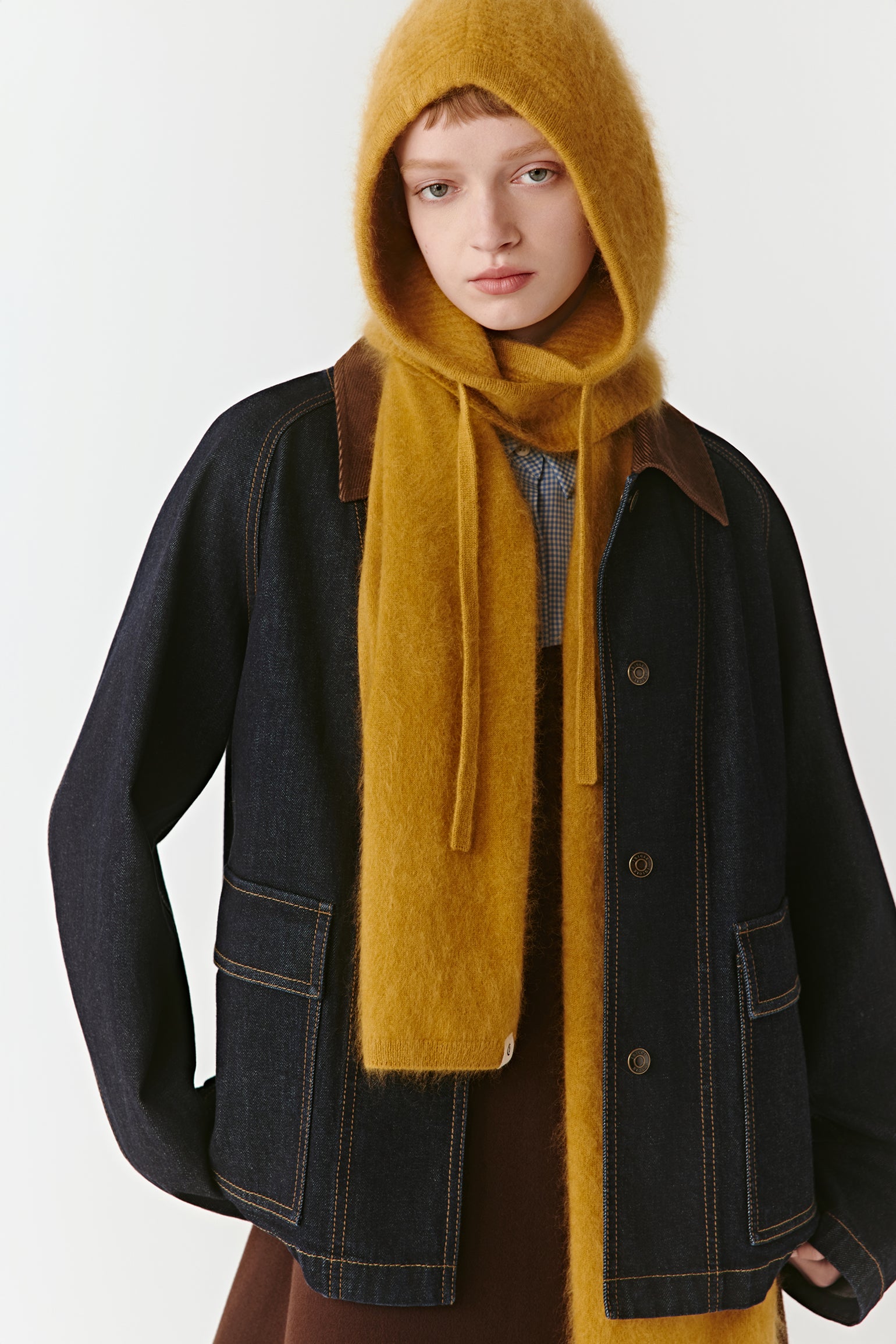 Side view of a mustard yellow knit hood and scarf styled with a black jacket on a light background