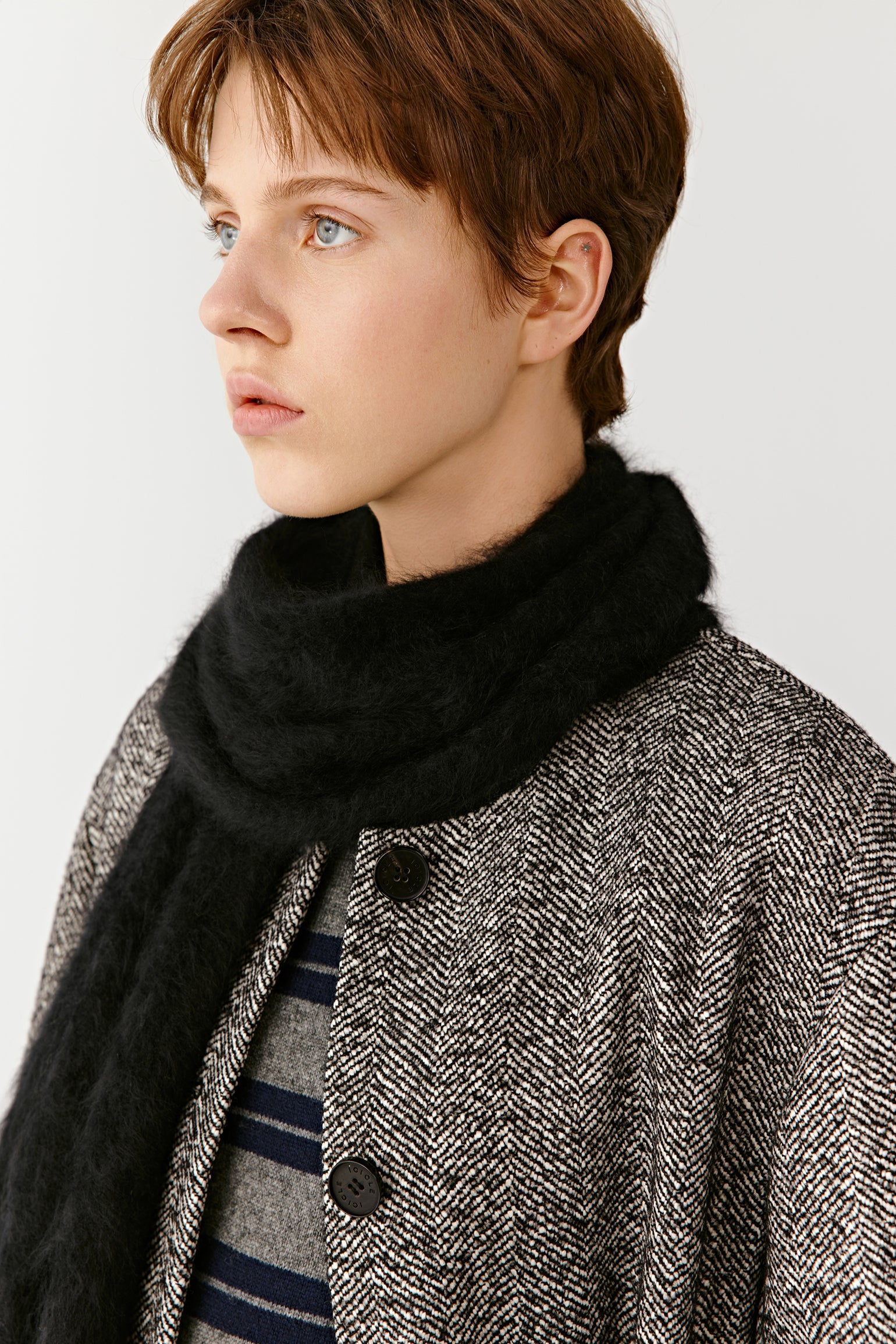 Side view of a woman wearing a grey coat and black scarf on a light background