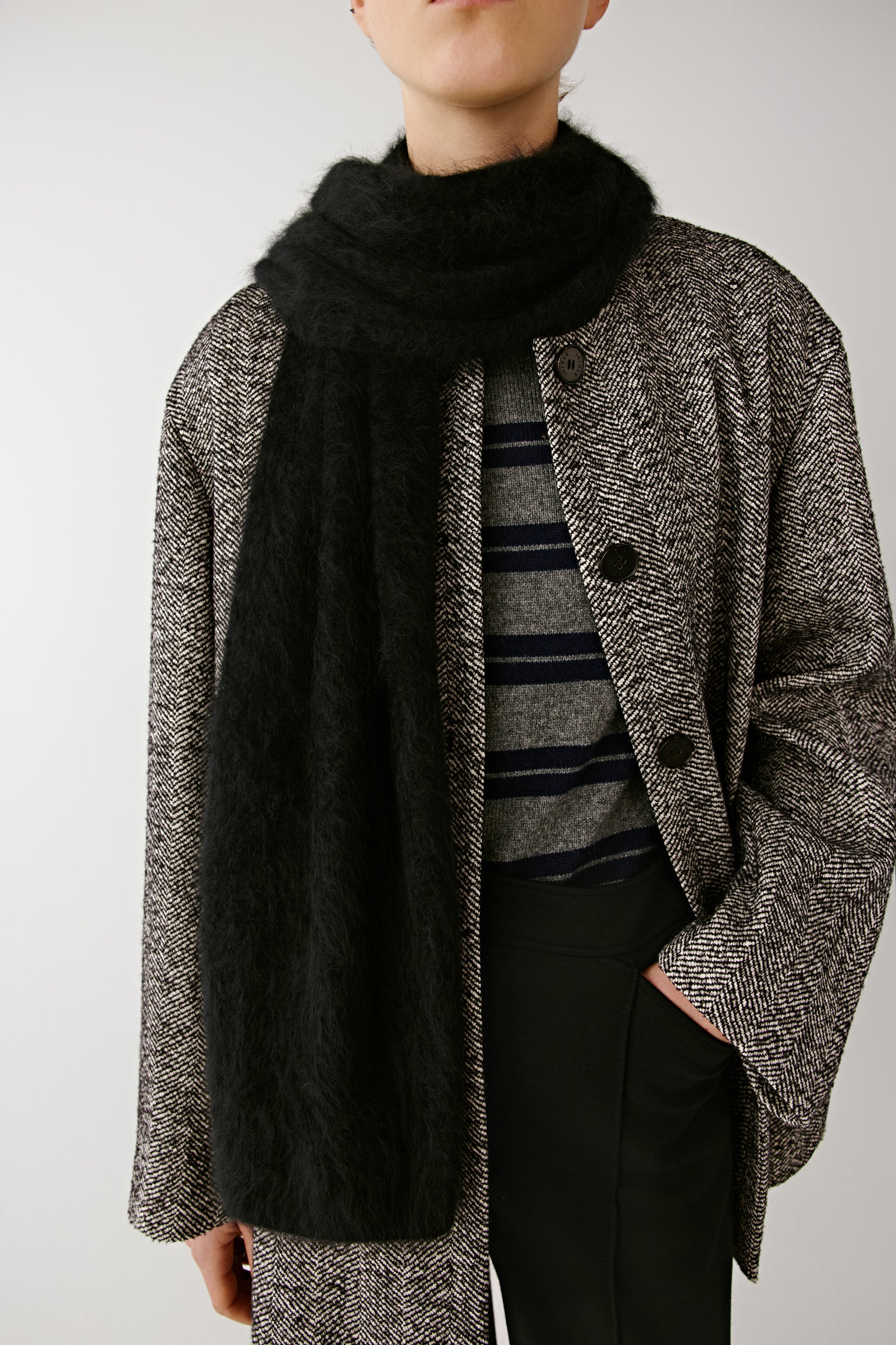 Woman wearing a grey textured coat with a black scarf over a striped top on a light background