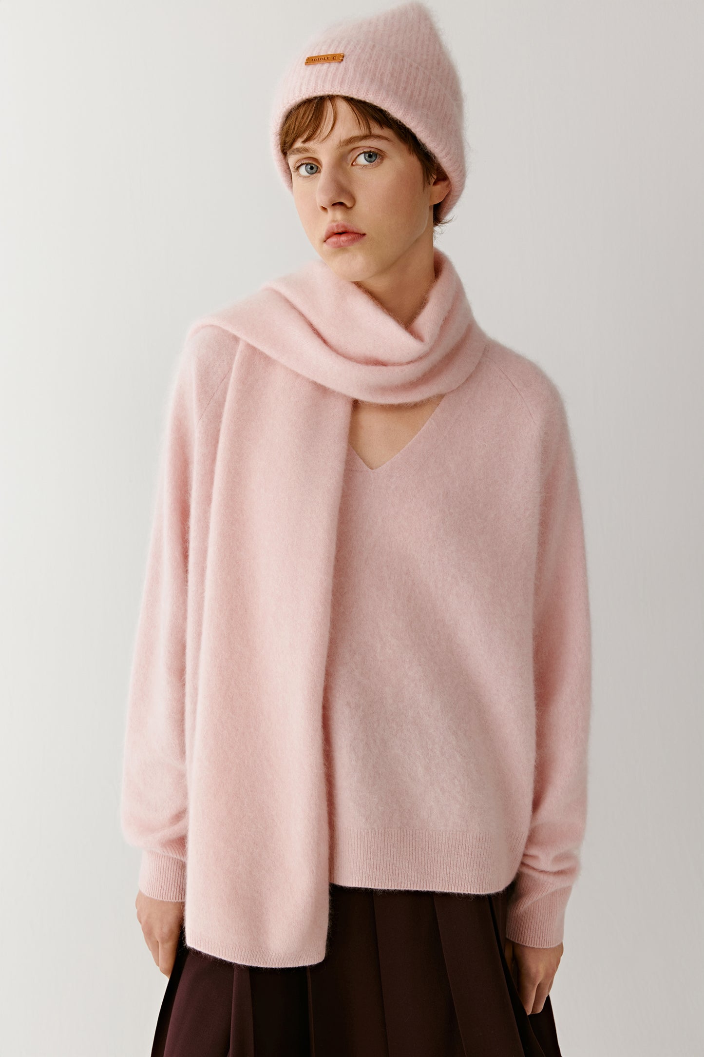 Woman wearing a soft pink knit beanie and matching scarf with a relaxed pink sweater on a light background