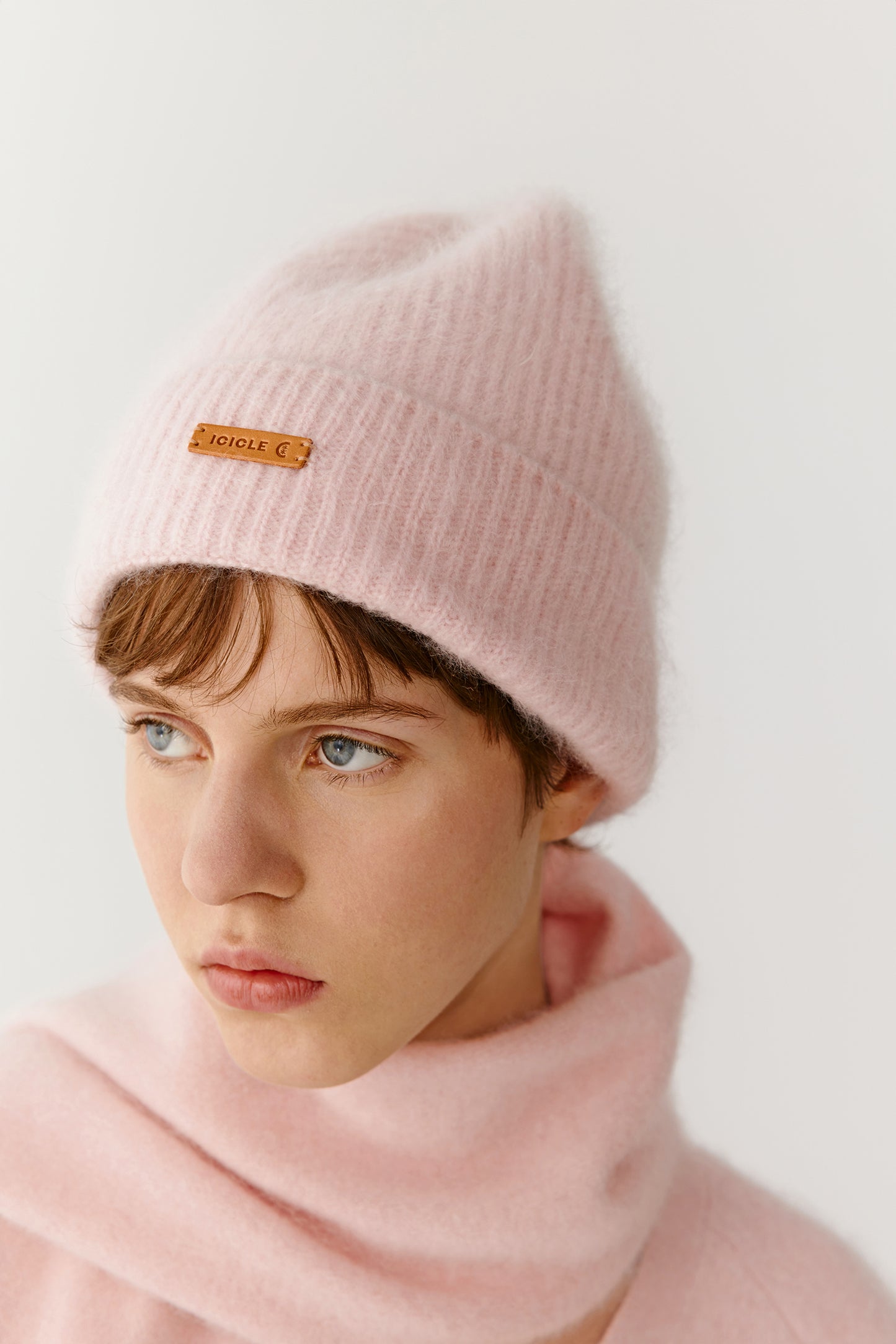 Front view of a woman wearing a light pink knit beanie and scarf on a light background