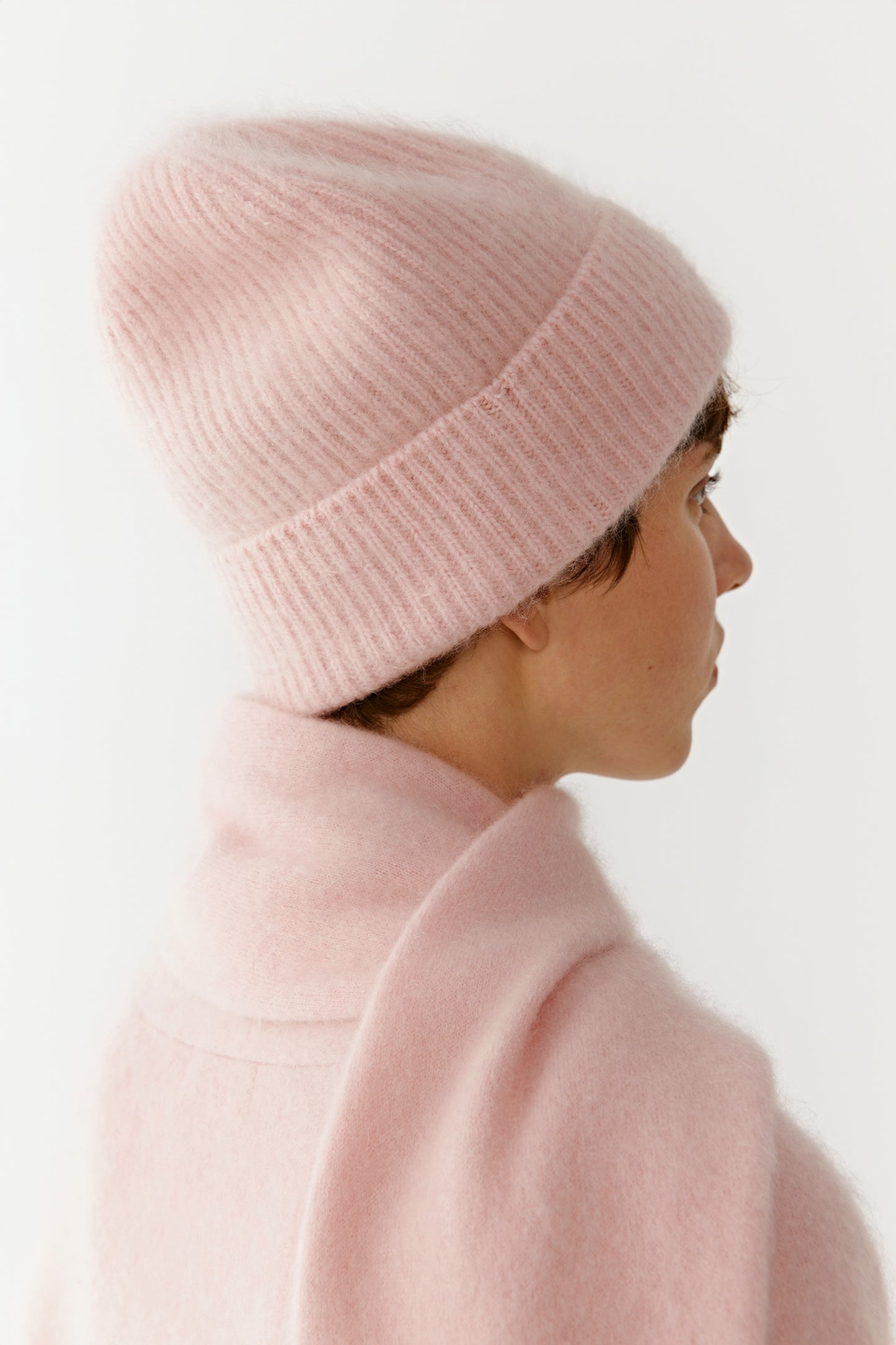 Side view of a woman wearing a pink knit beanie and scarf on a light background