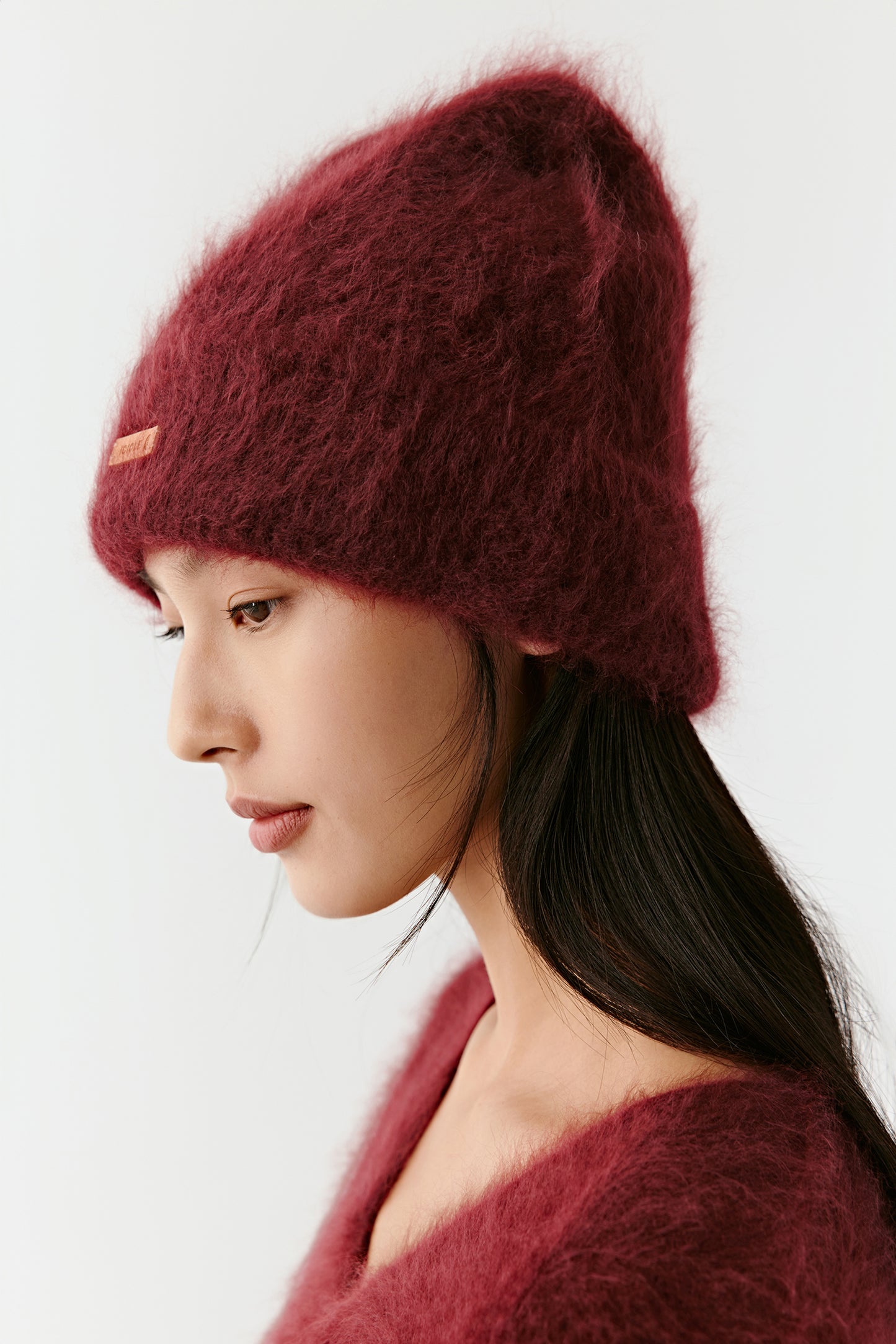 Side view of a woman wearing a burgundy knit beanie on a light background