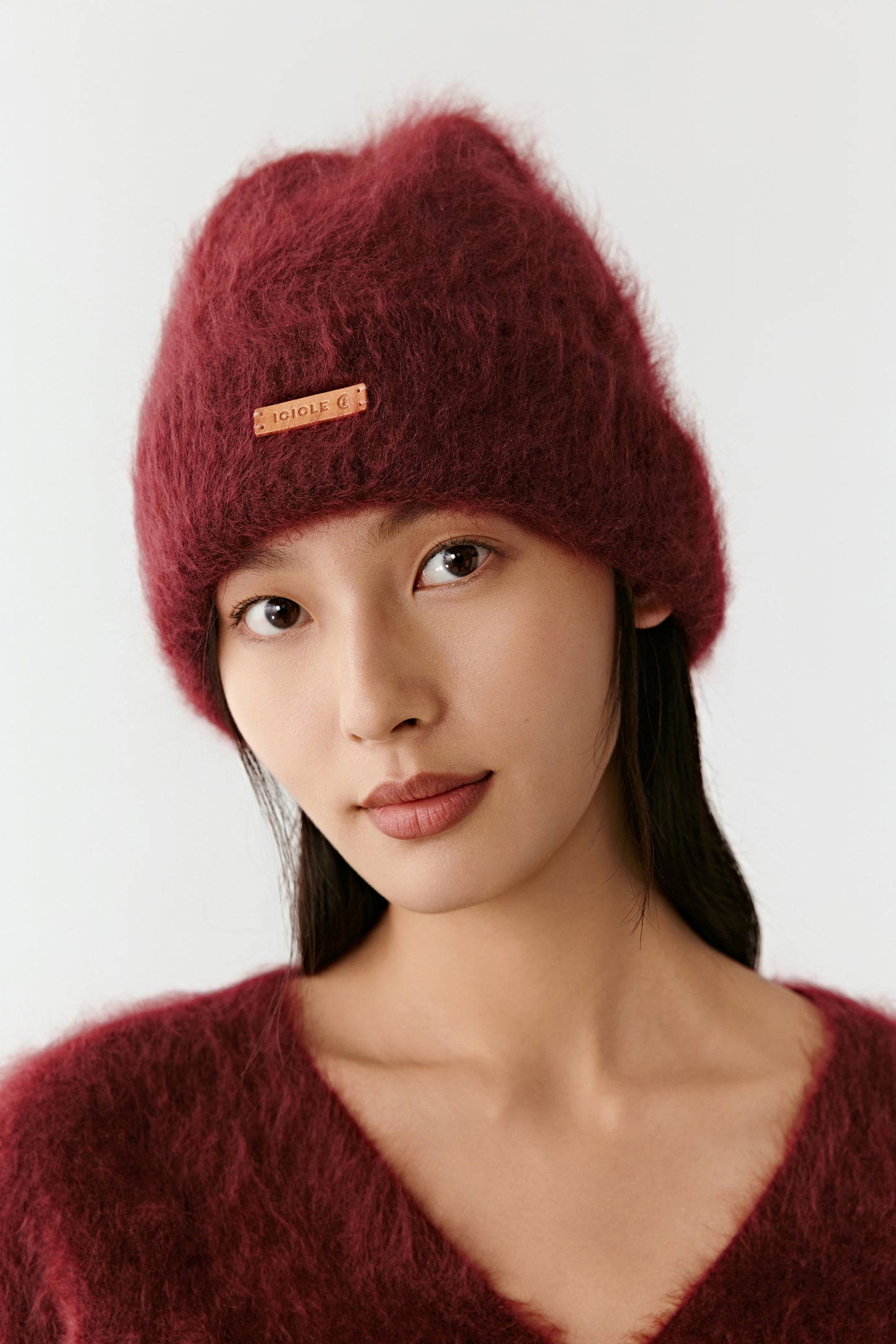 Woman wearing a burgundy knit beanie with a small leather logo on a light background