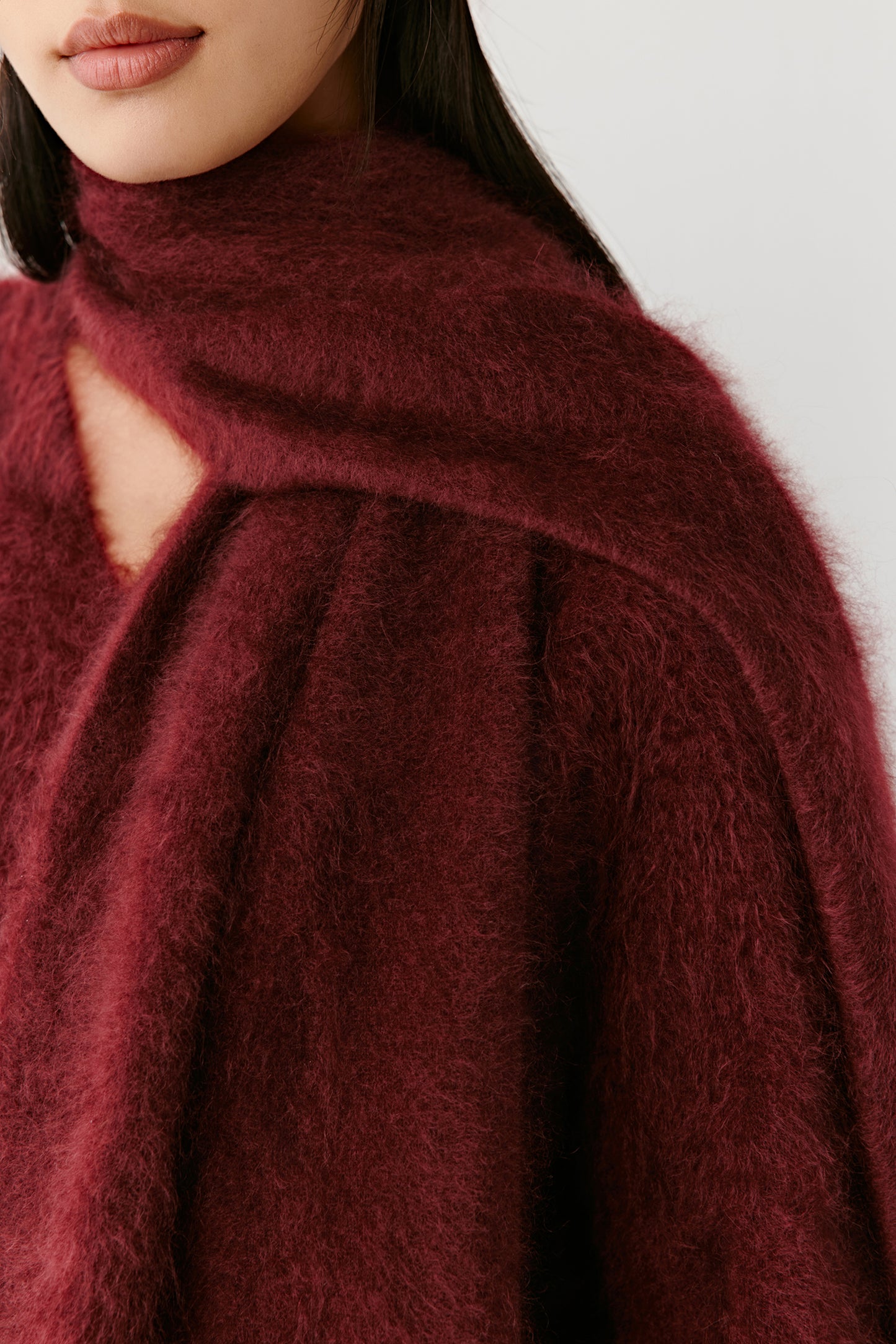 Detail view of a burgundy knit scarf with textured fabric on a light background
