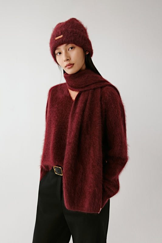 Woman wearing a burgundy knit beanie and matching scarf with a soft burgundy sweater on a light background