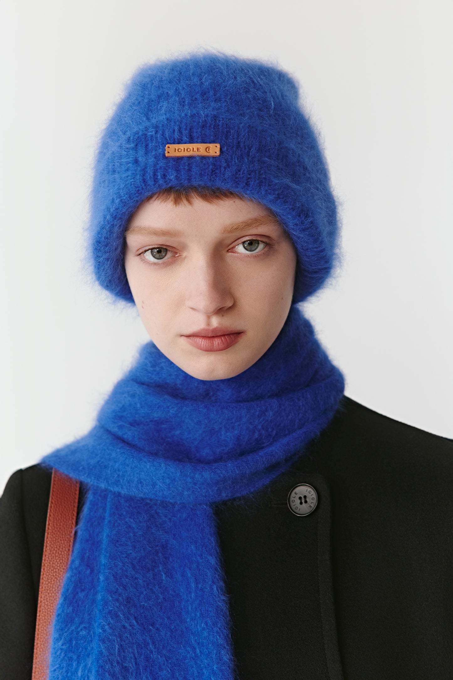 Woman wearing a bright blue knit beanie and matching scarf styled with a black coat on a light background