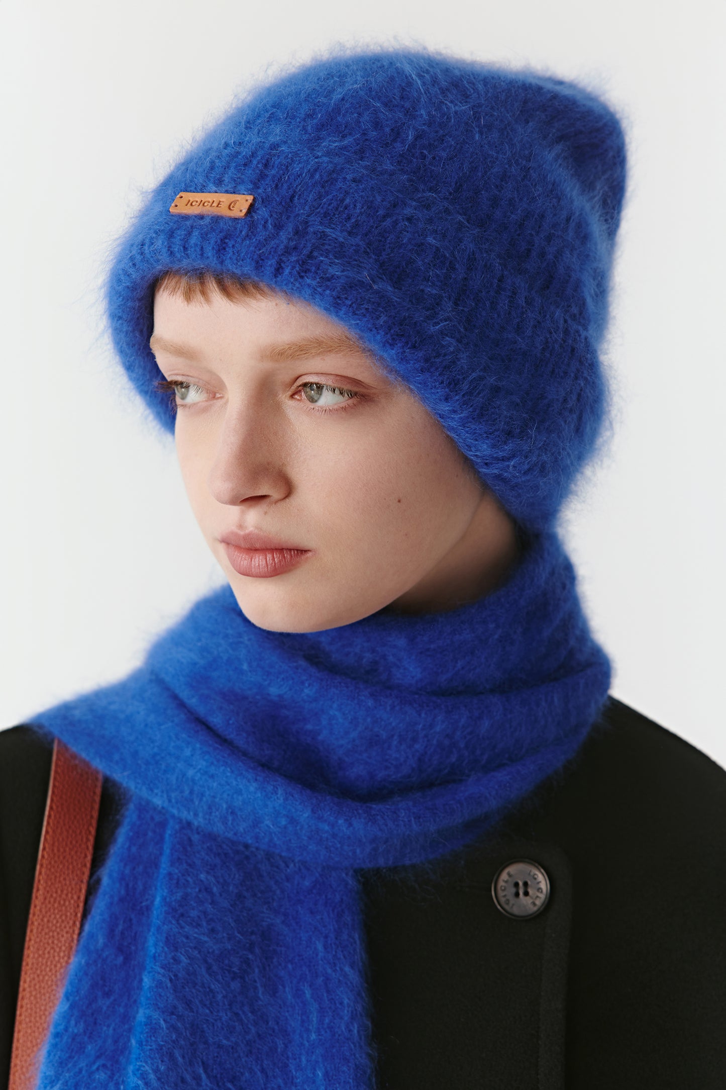 Side view of a woman wearing a bright blue knit beanie and matching scarf on a light background